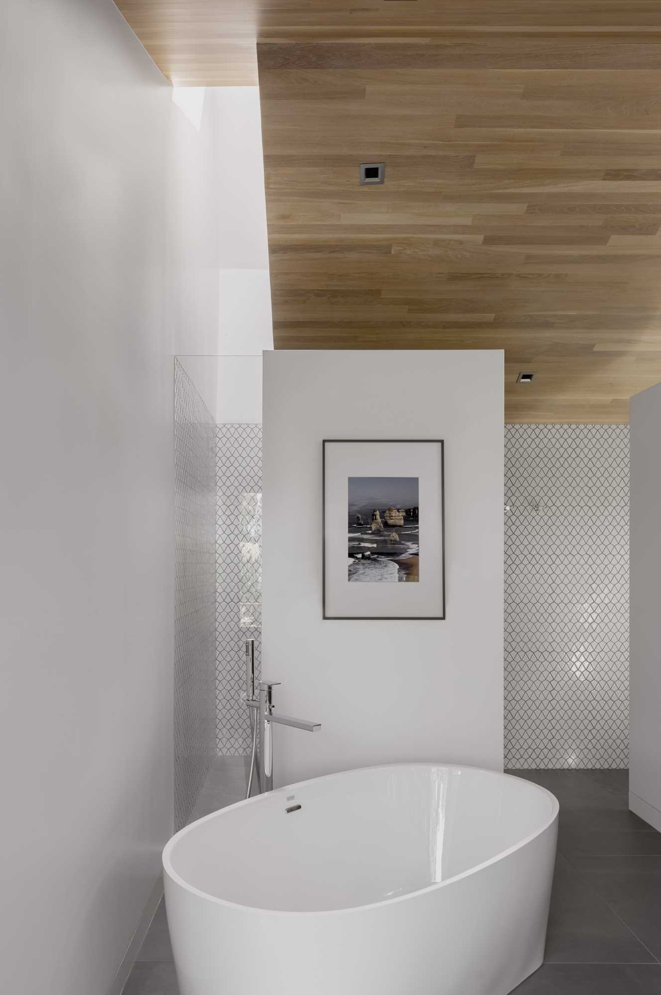 A remodeled bathroom has free-standing tub and south-facing vanity for two that are separated by a pair of part-height walls that allow light to spill over into a private walk-in shower area that is topped by a skylight and toilet room.