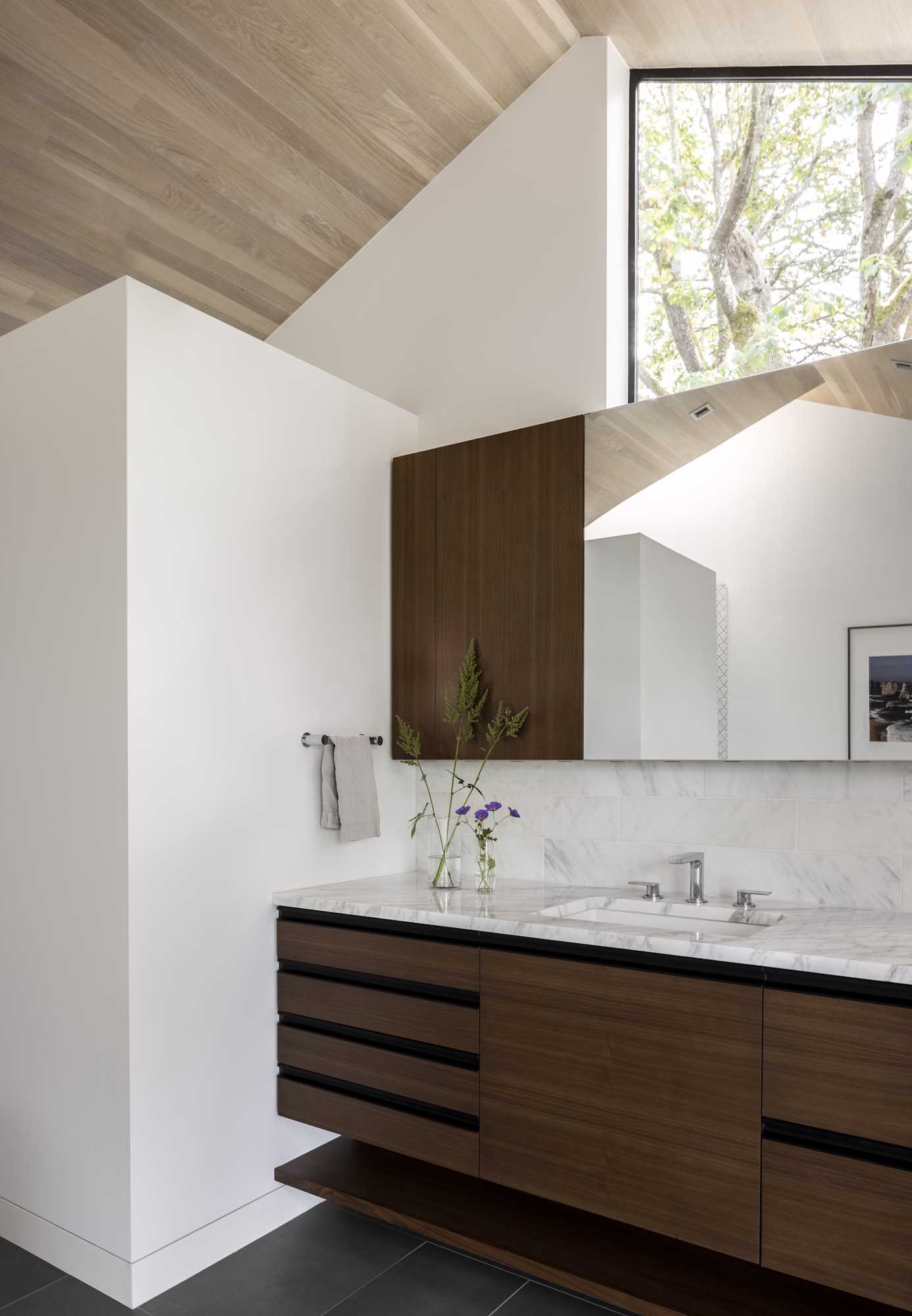 A remodeled bathroom has free-standing tub and south-facing vanity for two that are separated by a pair of part-height walls that allow light to spill over into a private walk-in shower area that is topped by a skylight and toilet room.