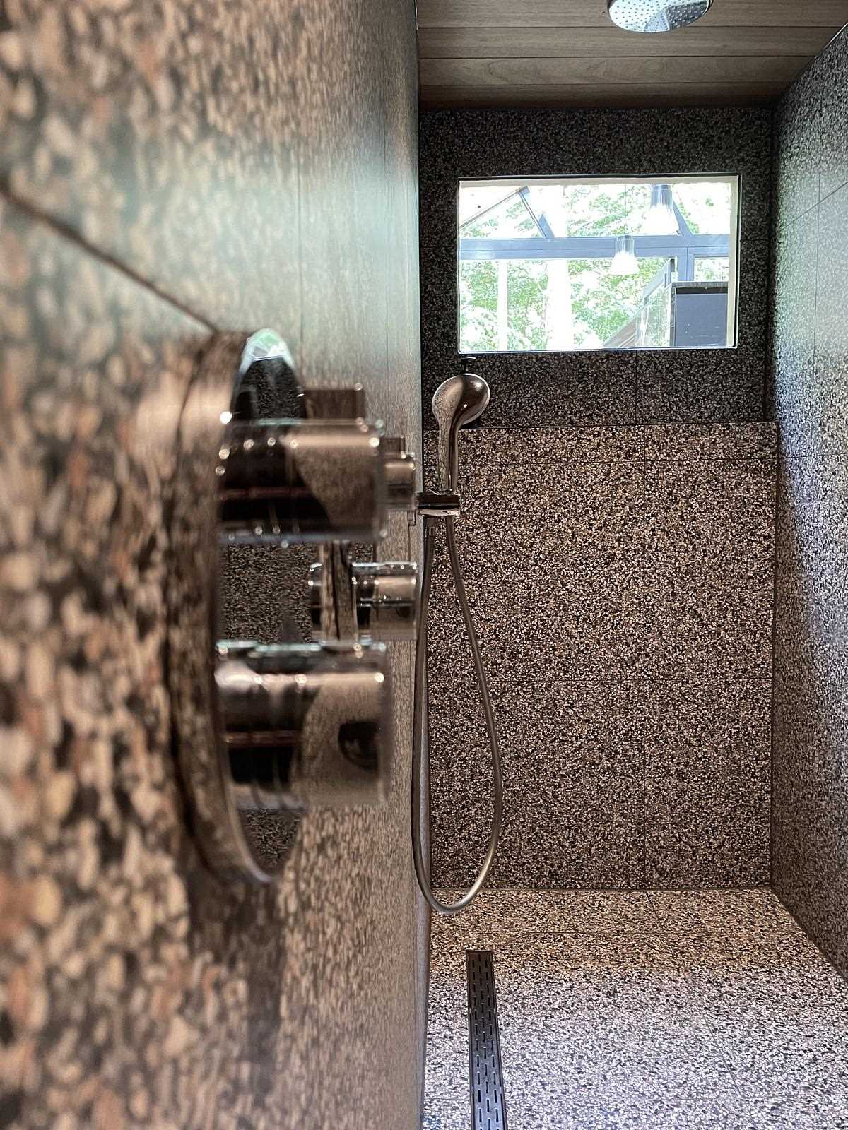 A shower with large format tiles and a window that looks out onto the living space.