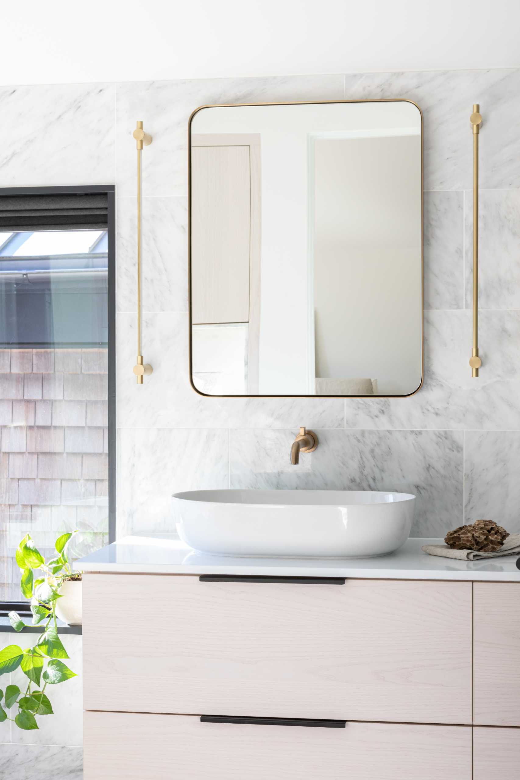 In this modern bathroom, there's wood cabinetry, a freestanding bathtub, dark floor tiles in a herringbone pattern, and metallic accents.