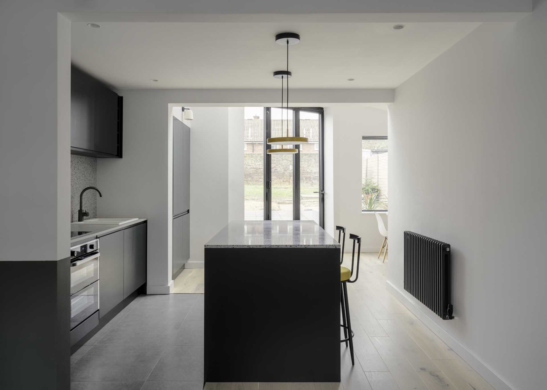 A kitchen with minimalist black cabinets and an island with seating. Yellow accents in the lights and chairs add a pop of color to the space.