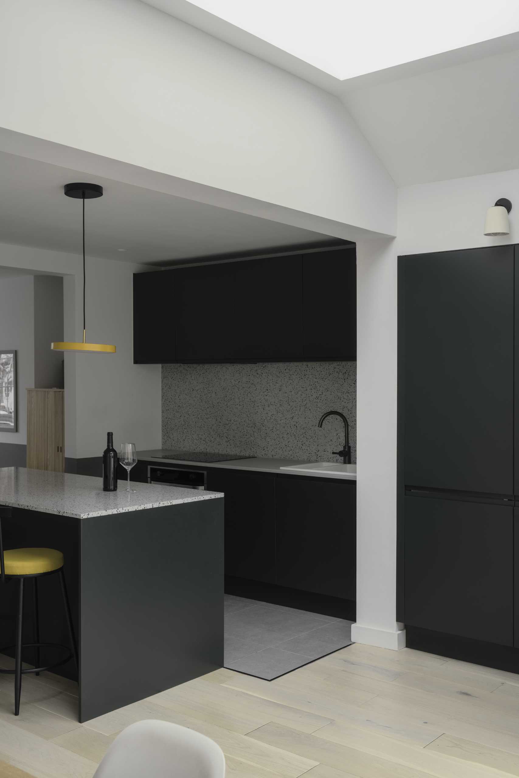 A kitchen with minimalist black cabinets and an island with seating. Yellow accents in the lights and chairs add a pop of color to the space.