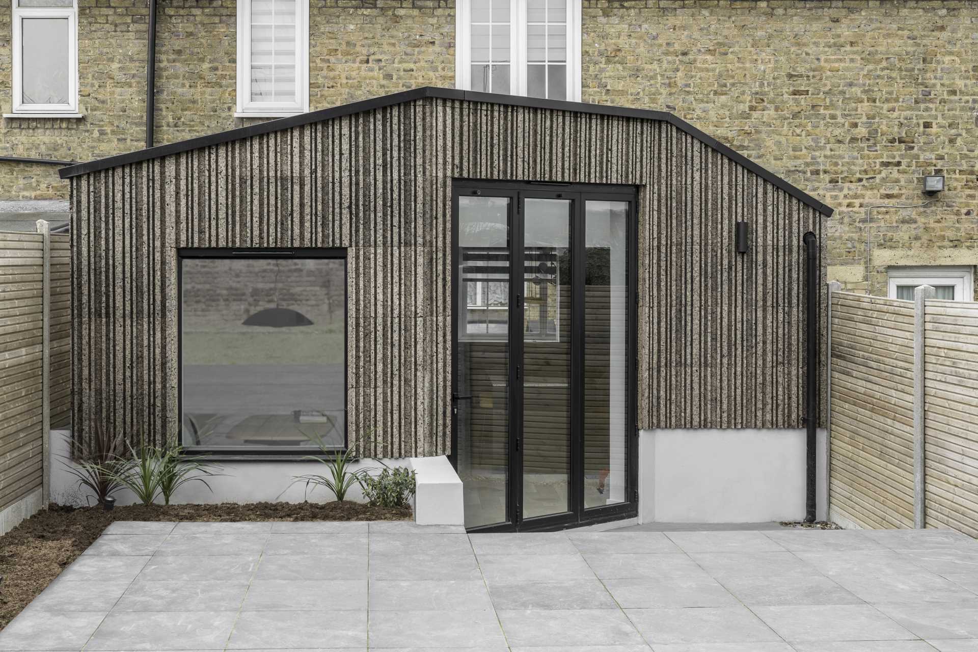 A modern home extension that's clad in patterned cork, and includes black window and door frames.