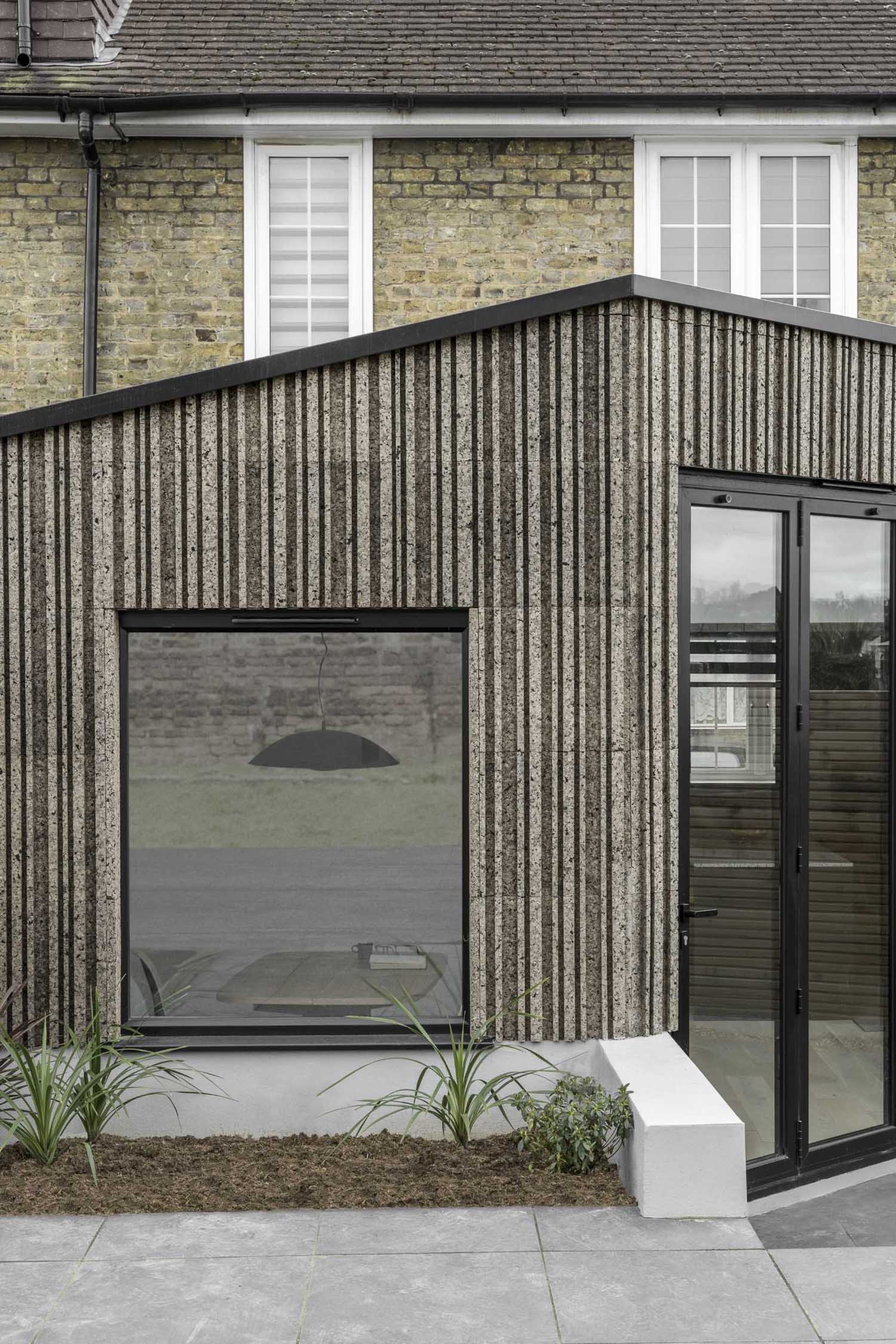 A modern home extension that's clad in patterned cork, and includes black window frames.