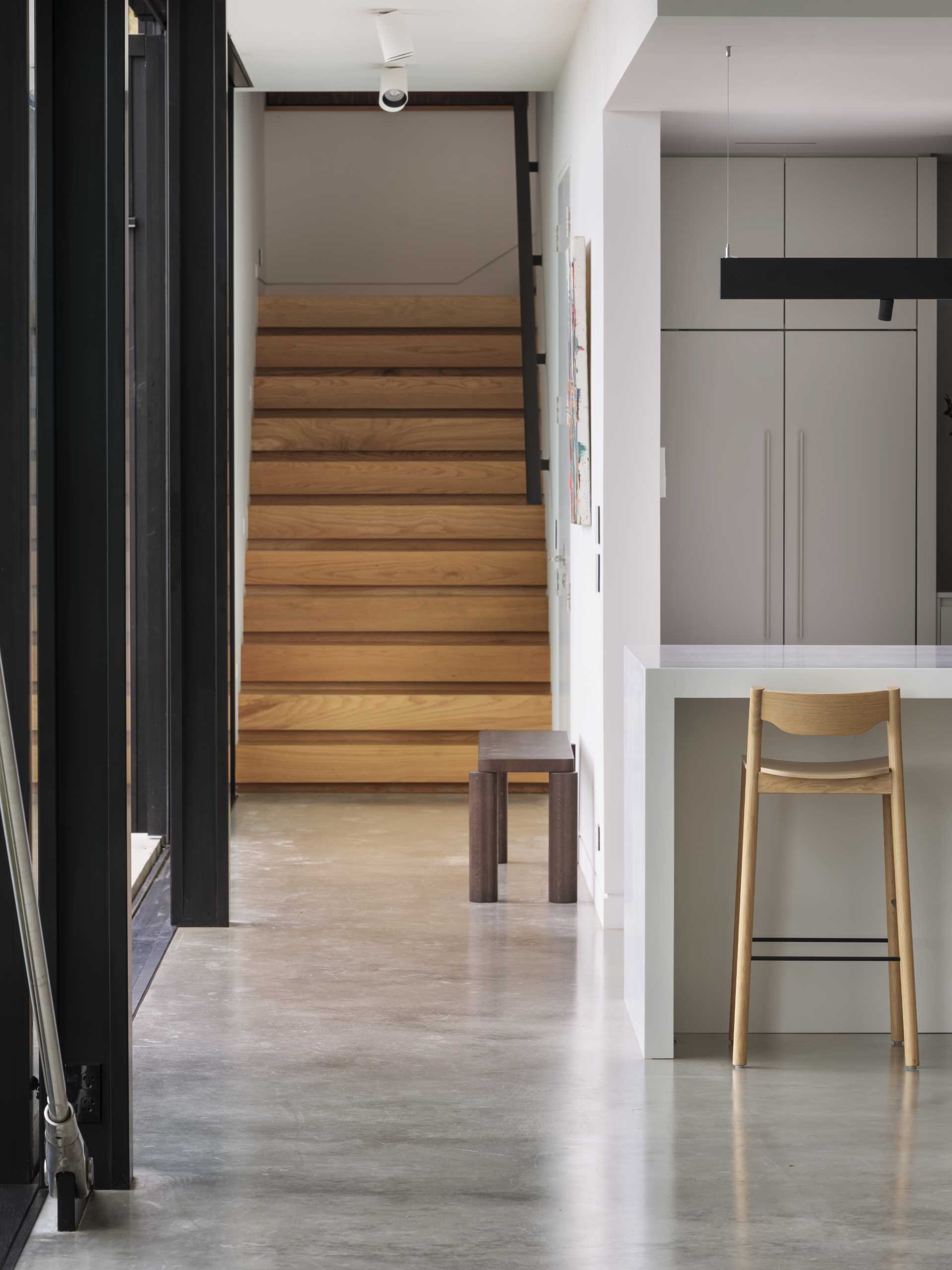 A modern home with a white kitchen and wood stairs leading to the upper level of the home.