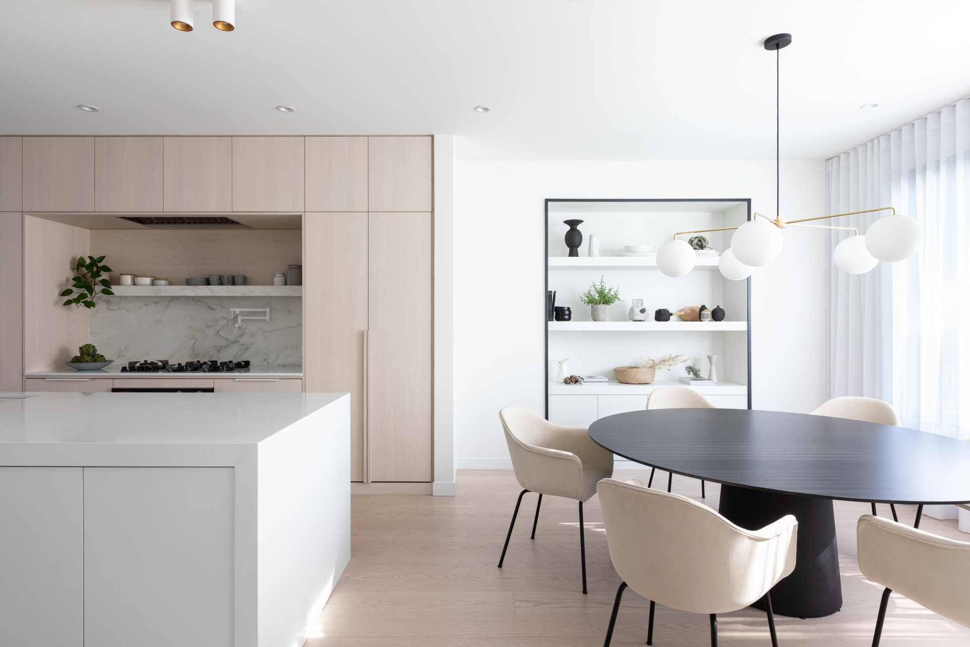 In this dining area, which is located next to the kitchen, there's a round table and a built-in display niche with black accents, which in combination with matte white shelves creates a striking display for objects.