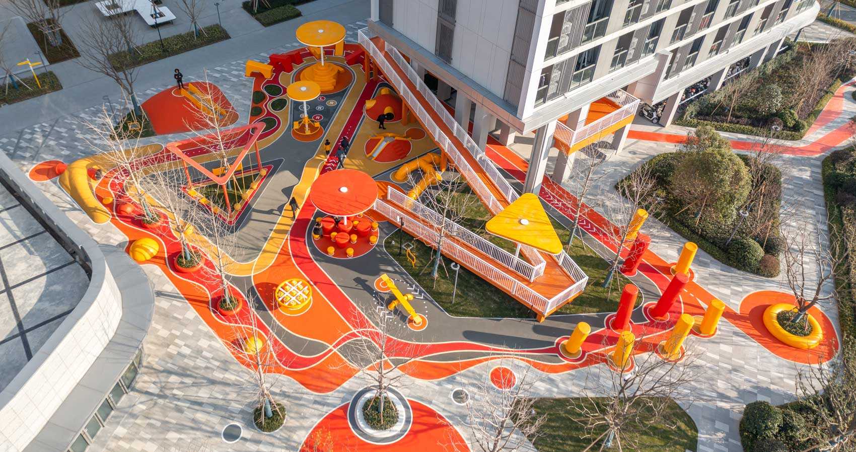 A modern and colorful landscaped park with slides, pathways, a merry-go-round, lounge seating, seesaw, shading structures, seating, swings, and an amphitheater.