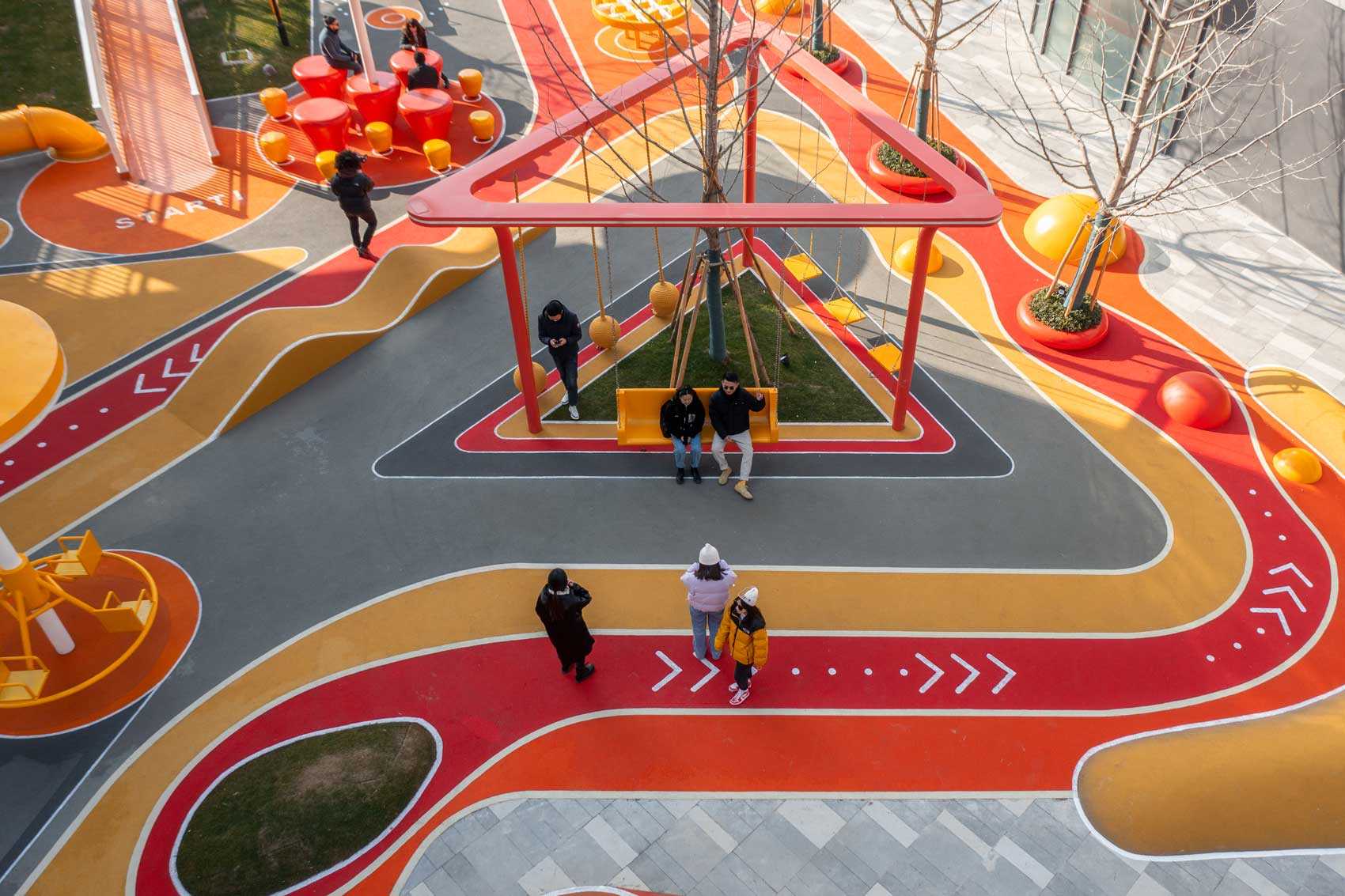 A modern and colorful landscaped park with slides, pathways, a merry-go-round, lounge seating, seesaw, shading structures, seating, swings, and an amphitheater.