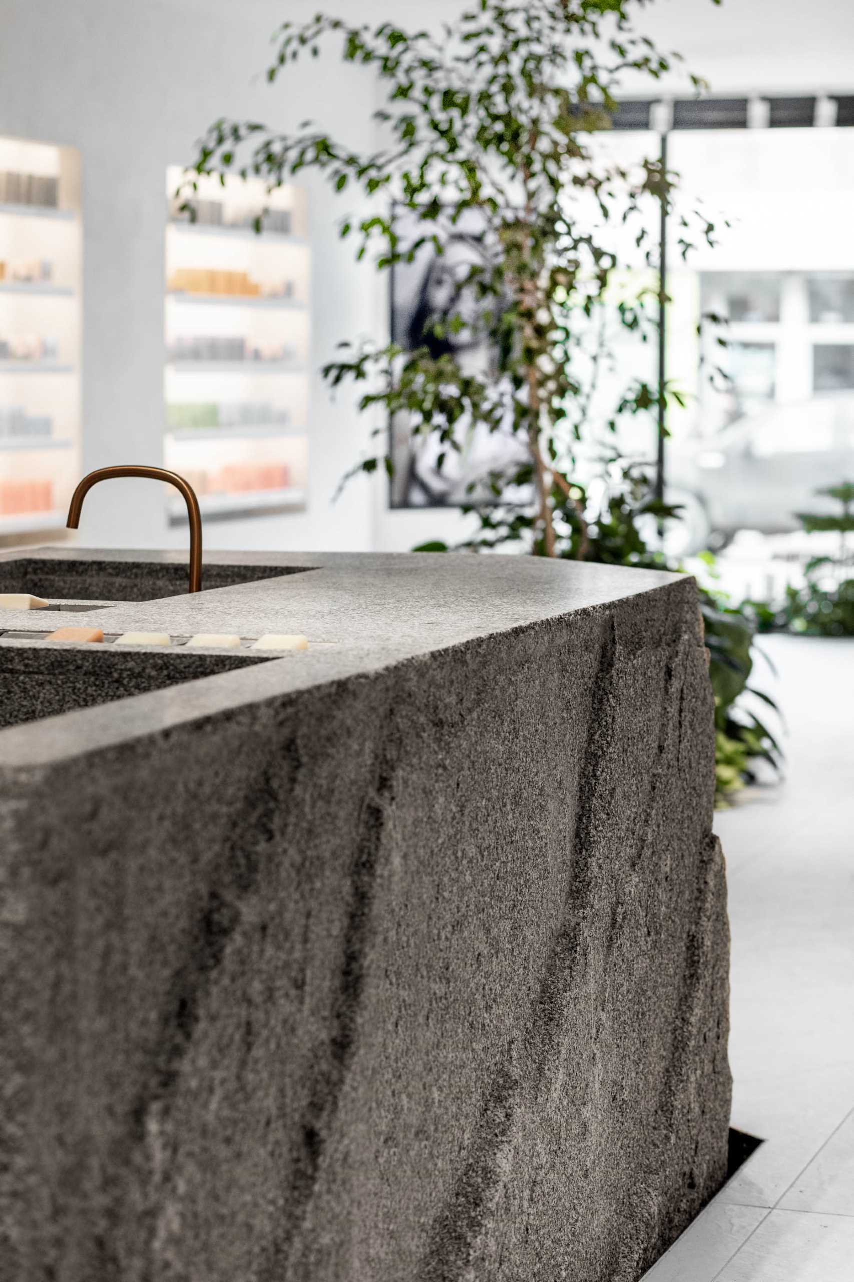 A modern retail store for a beauty brand includes a large boulder-like granite island with carved-out sinks.