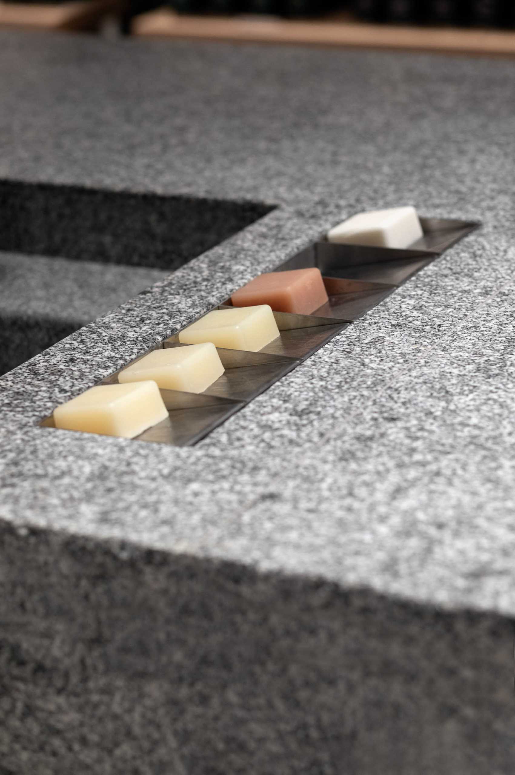 A modern retail store for a beauty brand includes a large boulder-like granite island with carved-out sinks and metal soap trays.