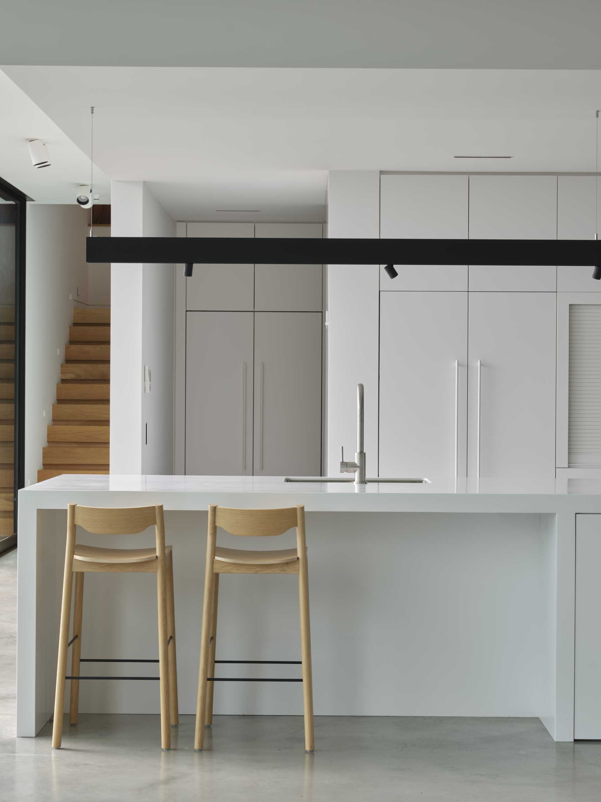 A minimalist white kitchen with a large island an concrete floor.