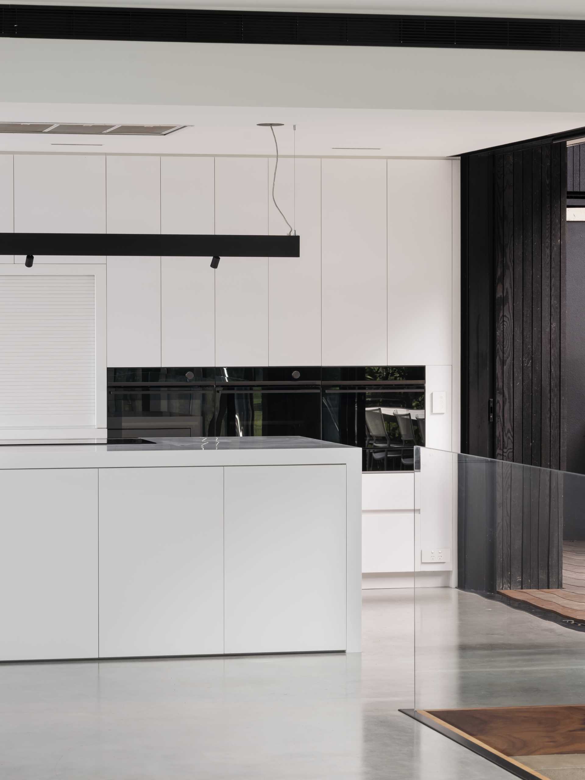 A minimalist white kitchen with a large island an concrete floor.