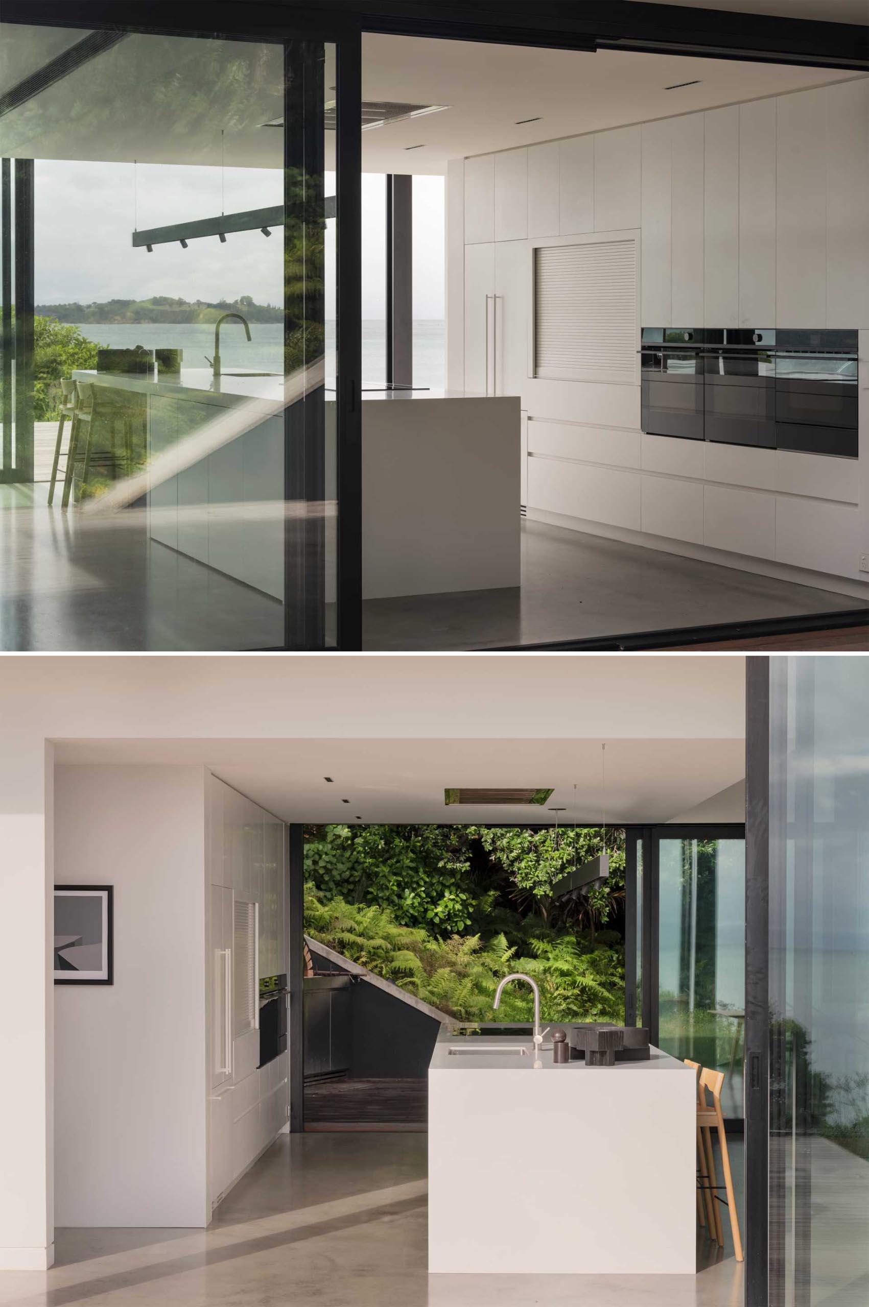 A minimalist white kitchen with a large island an concrete floor.