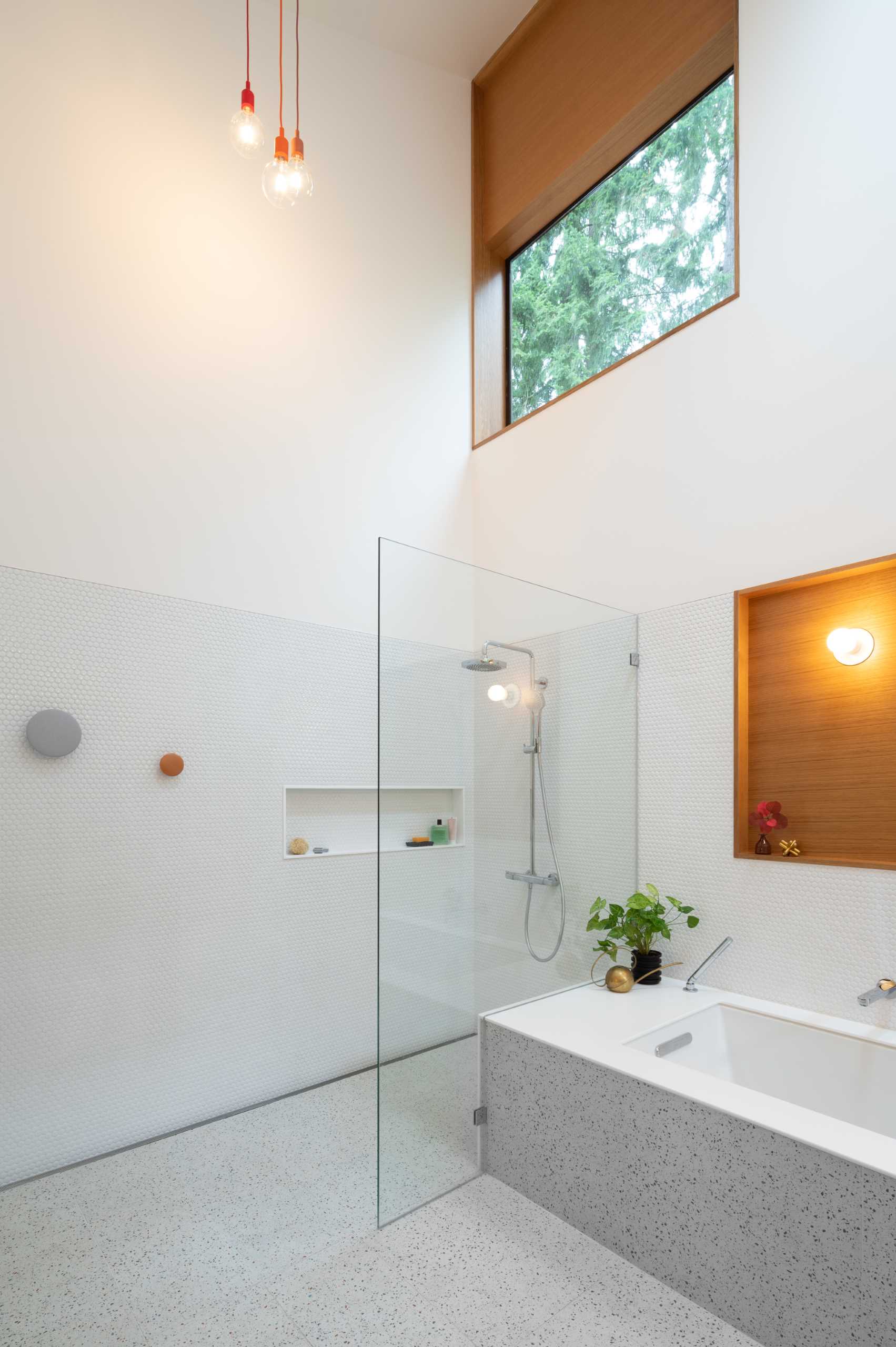 یک حمام مدرن با دیوارهای پوشیده از کاشی‌های پنی سفید، یک وان حمام توکار، و دوش با طاقچه قفسه‌بندی.