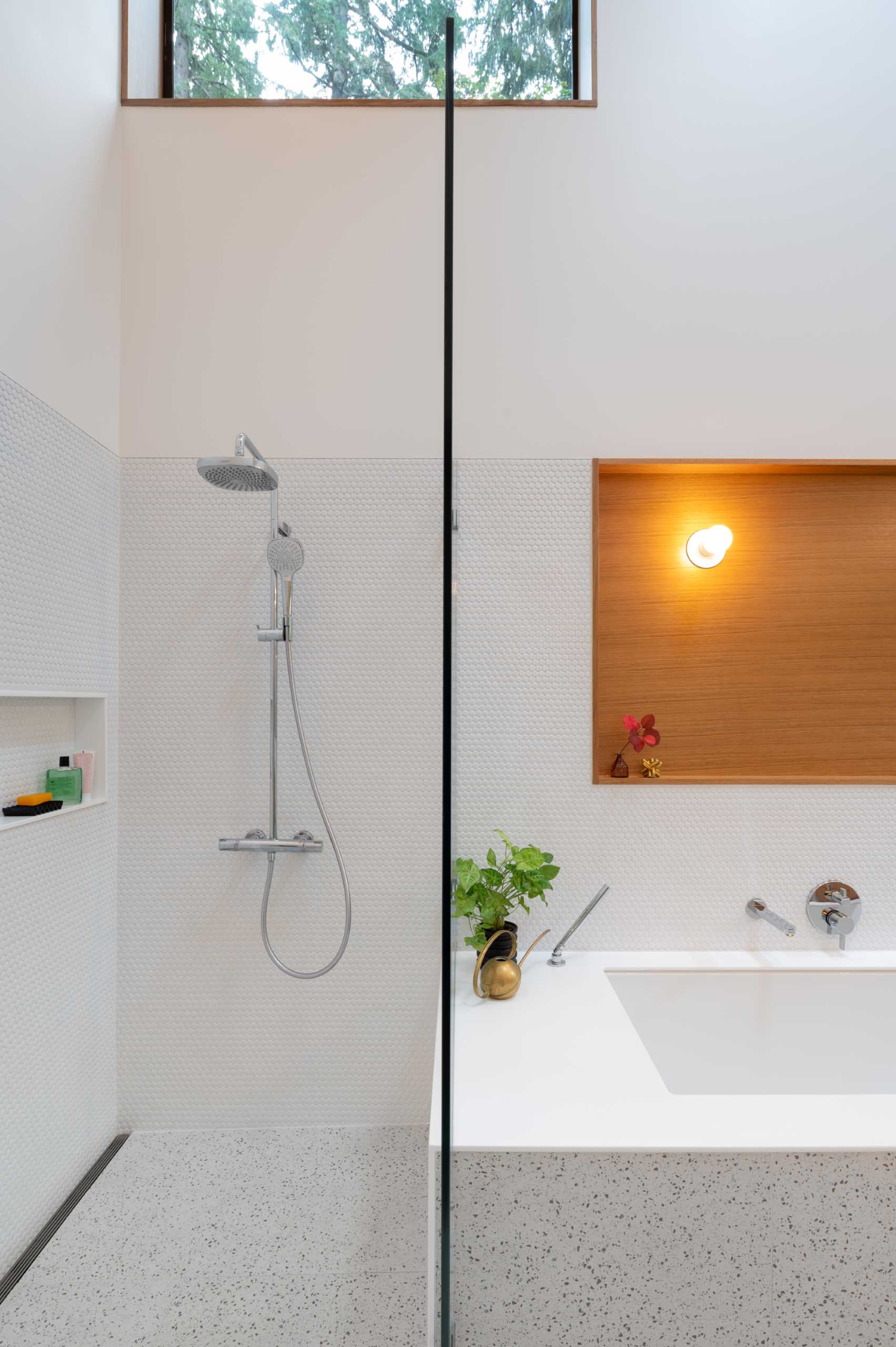 یک حمام مدرن با دیوارهای پوشیده از کاشی‌های پنی سفید، یک وان حمام توکار، و دوش با طاقچه قفسه‌بندی.