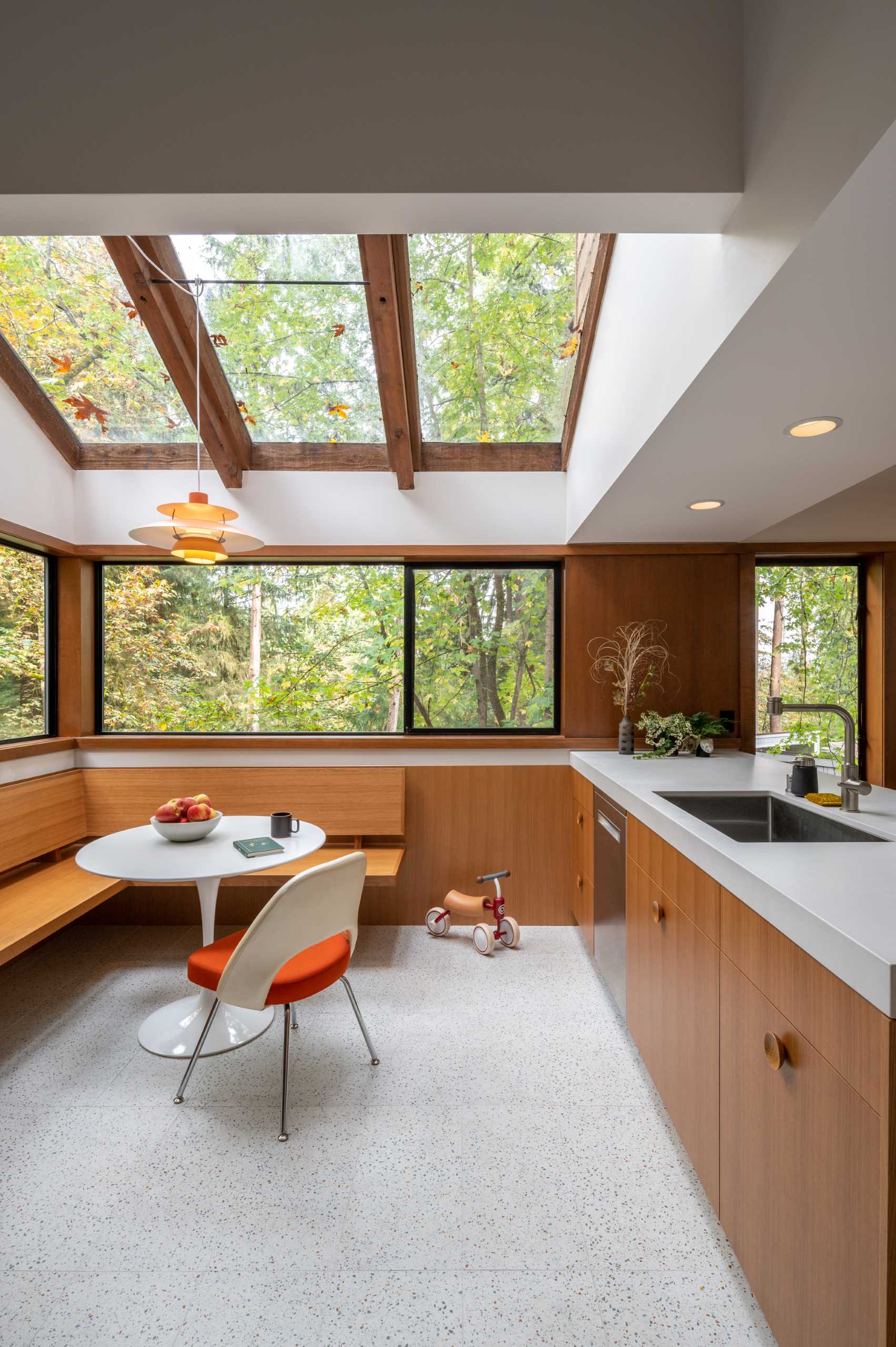 A remodeled kitchen with a built-in corner breakfast nook underneath the skylights and next to windows with forest views.