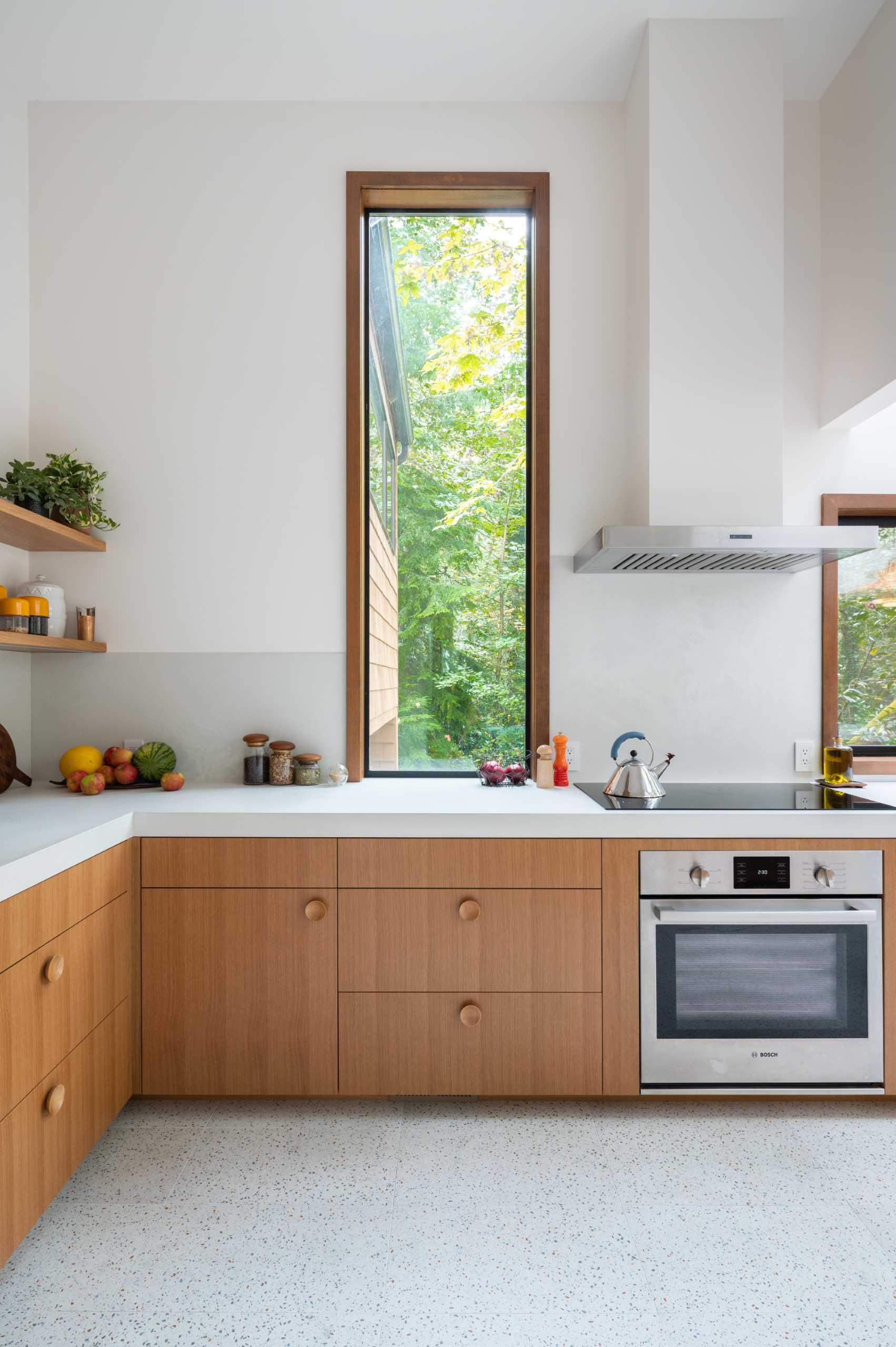 آشپزخانه ای بازسازی شده با کابینت های چوبی، میزهای ضخیم، و پنجره های بلند.