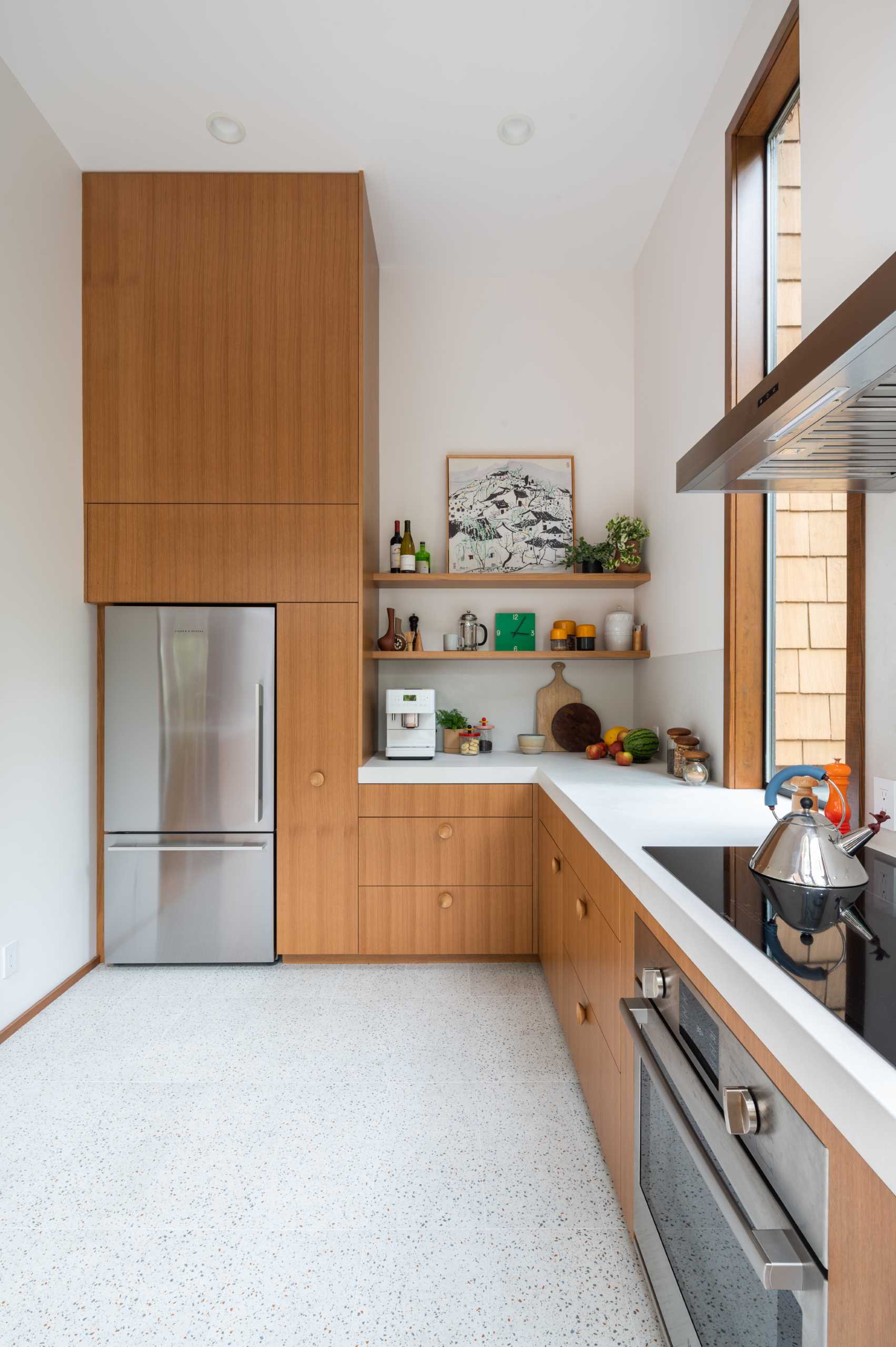 A remodeled kitchen with wood cabinets and shelves, thick countertops, and tall windows.
