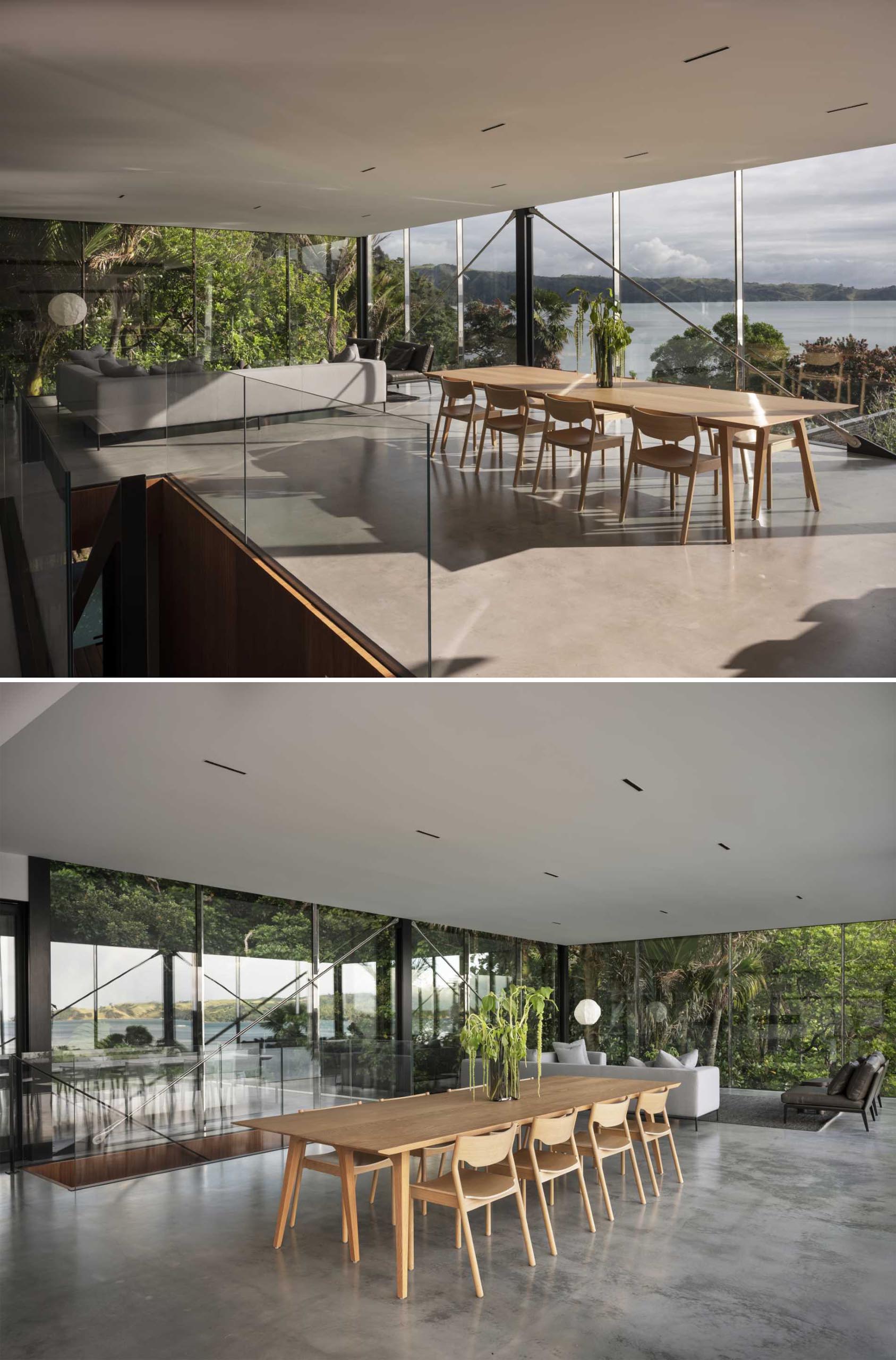 در این خانه مدرن با دیوارهای شیشه‌ای، یک ناهارخوری با پلان باز وجود دارد که با یک میز چوبی بزرگ و صندلی‌های همسان مبله شده است.