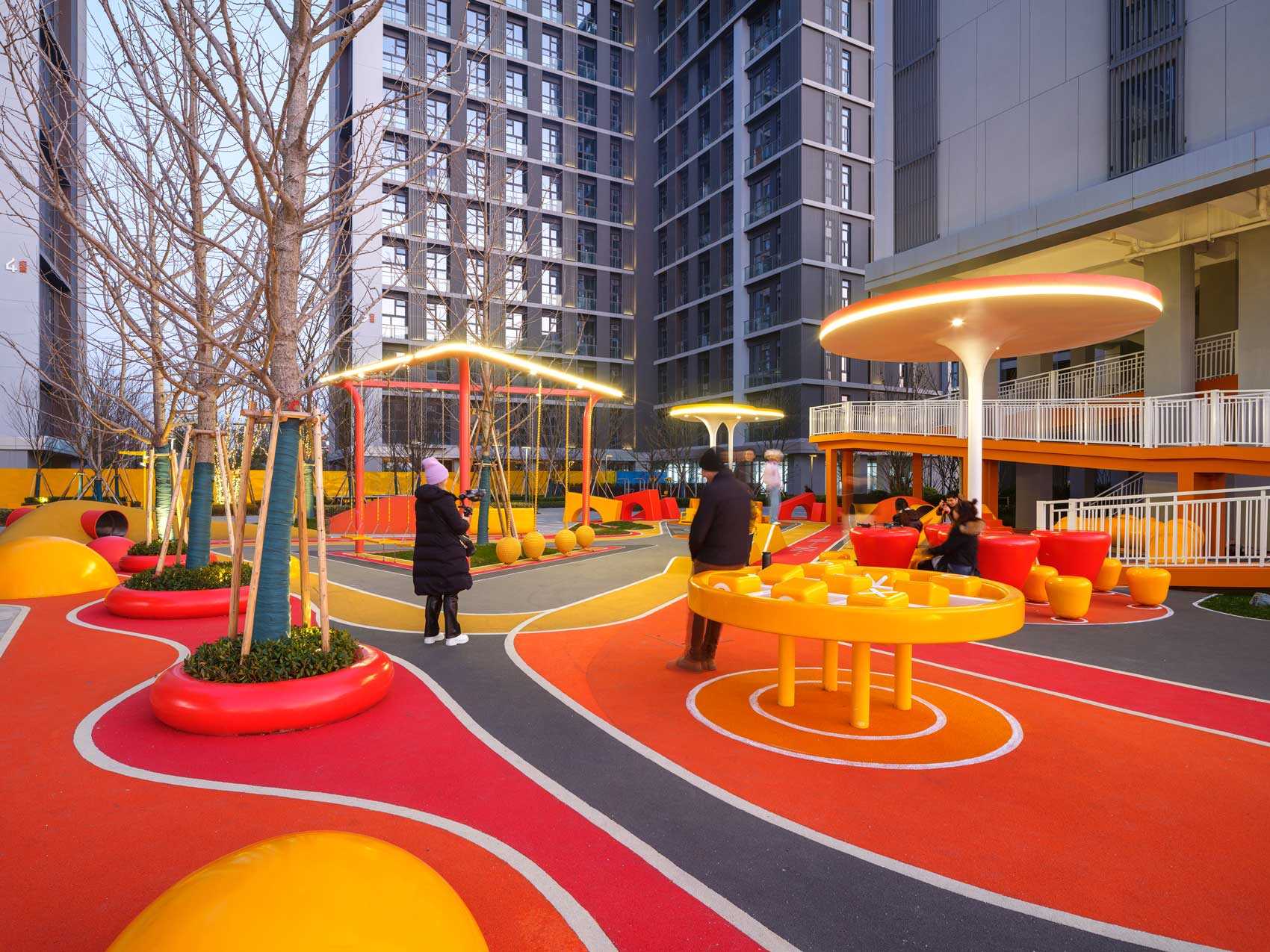 A modern and colorful landscaped park with slides, pathways, a merry-go-round, lounge seating, seesaw, shading structures, seating, swings, and an amphitheater.