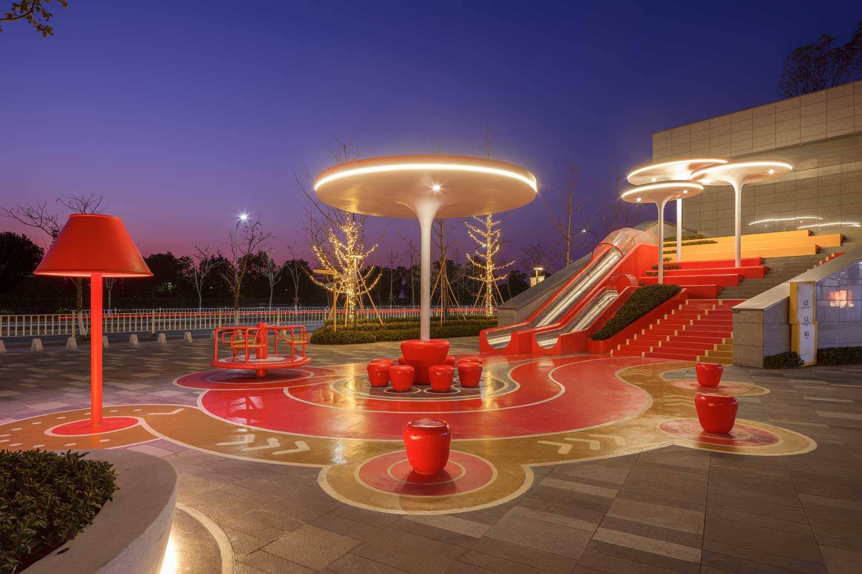 A modern and colorful landscaped park with slides, pathways, a merry-go-round, lounge seating, seesaw, shading structures, seating, swings, and an amphitheater.