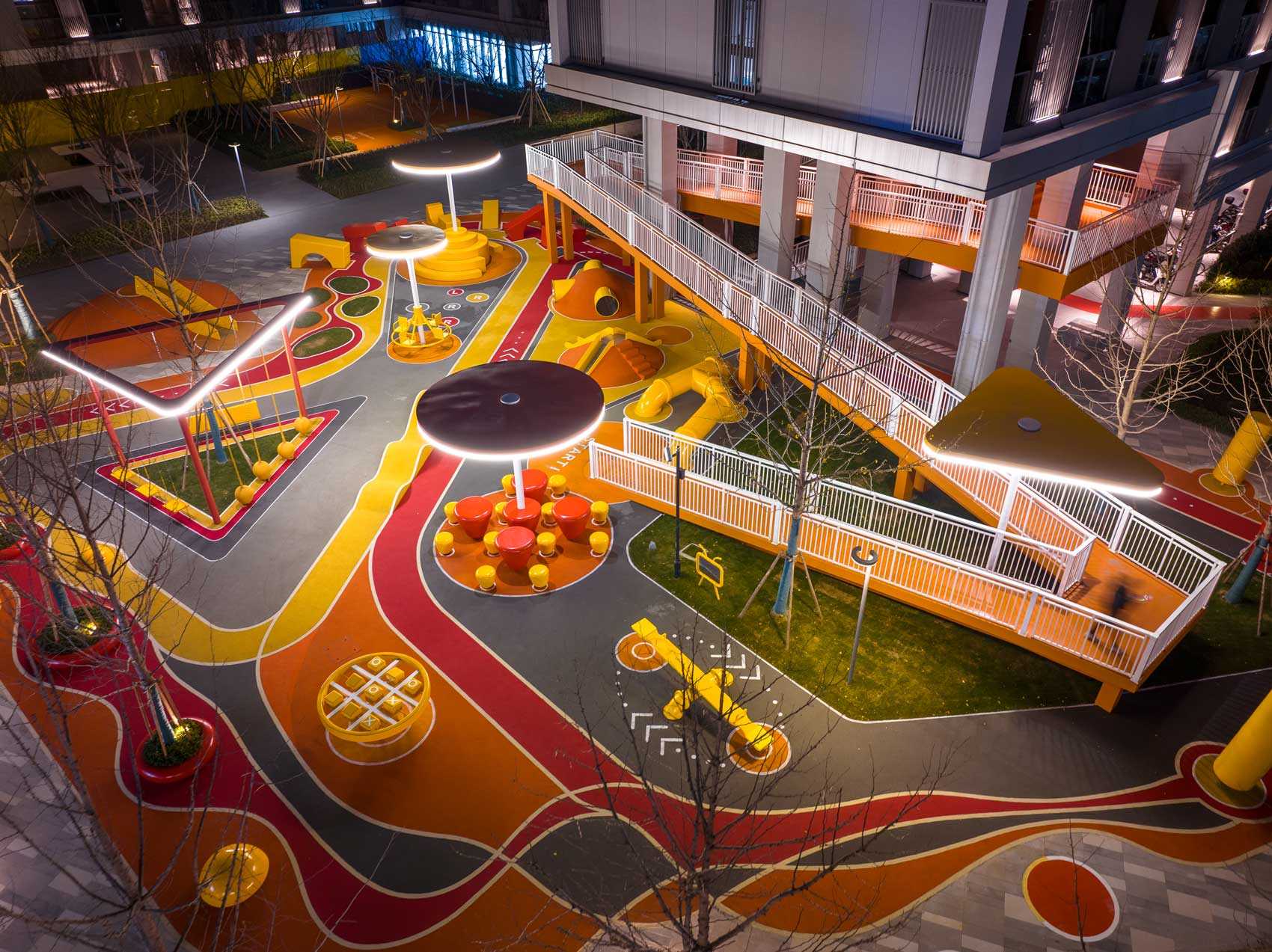 A modern and colorful landscaped park with slides, pathways, a merry-go-round, lounge seating, seesaw, shading structures, seating, swings, and an amphitheater.