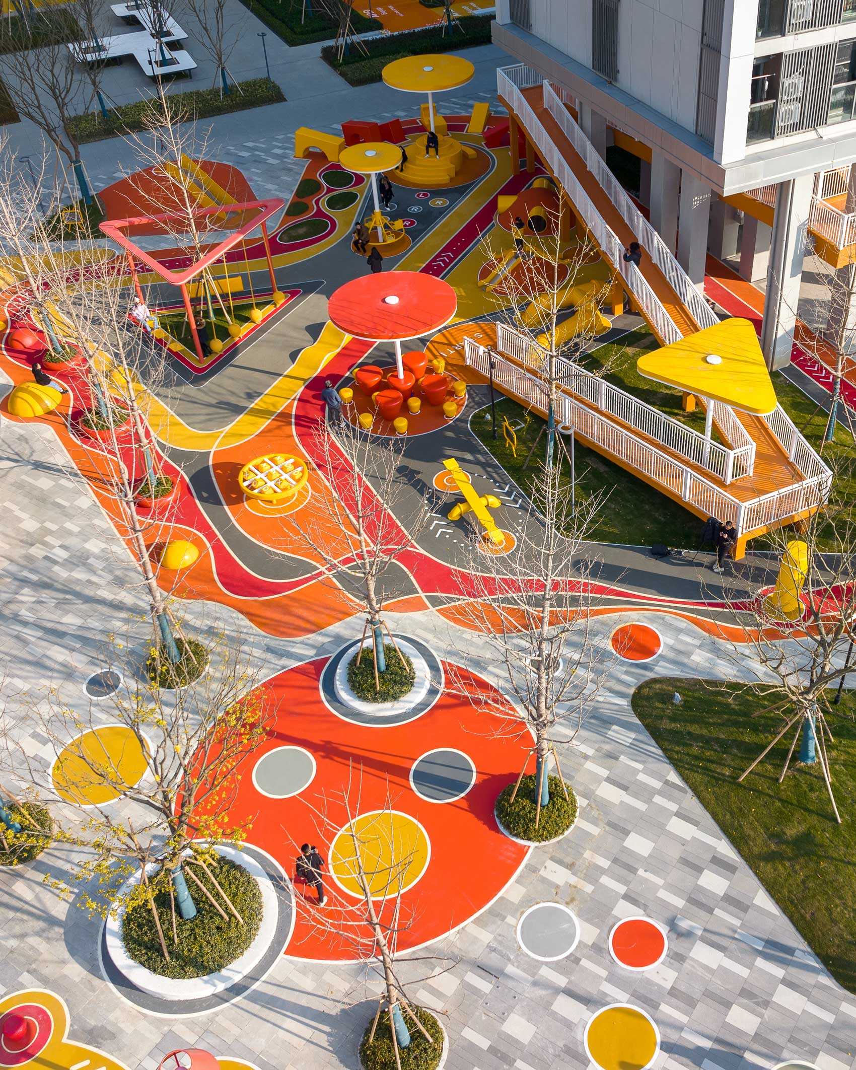 A modern and colorful landscaped park with slides, pathways, a merry-go-round, lounge seating, seesaw, shading structures, seating, swings, and an amphitheater.