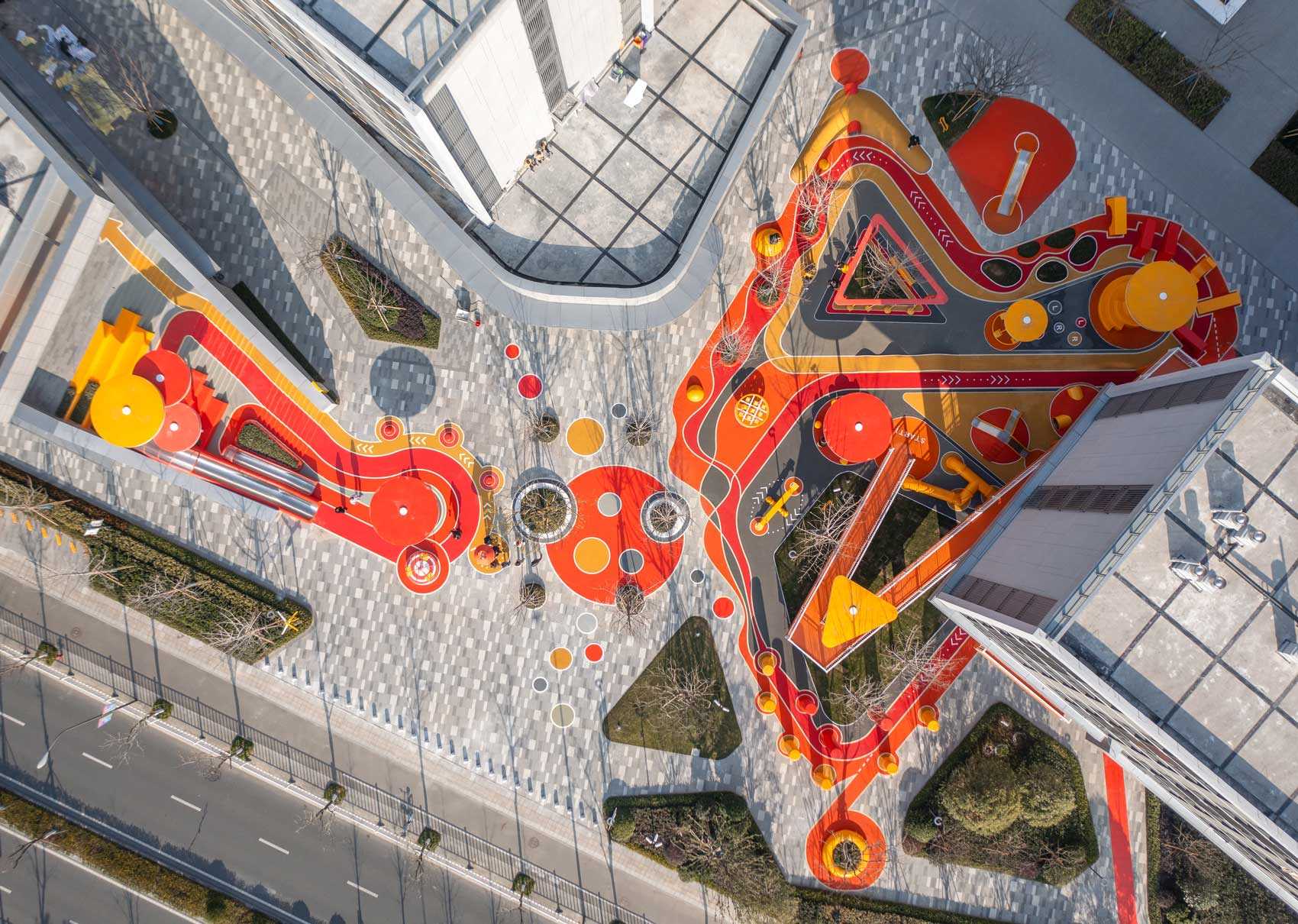 A modern and colorful landscaped park with slides, pathways, a merry-go-round, lounge seating, seesaw, shading structures, seating, swings, and an amphitheater.
