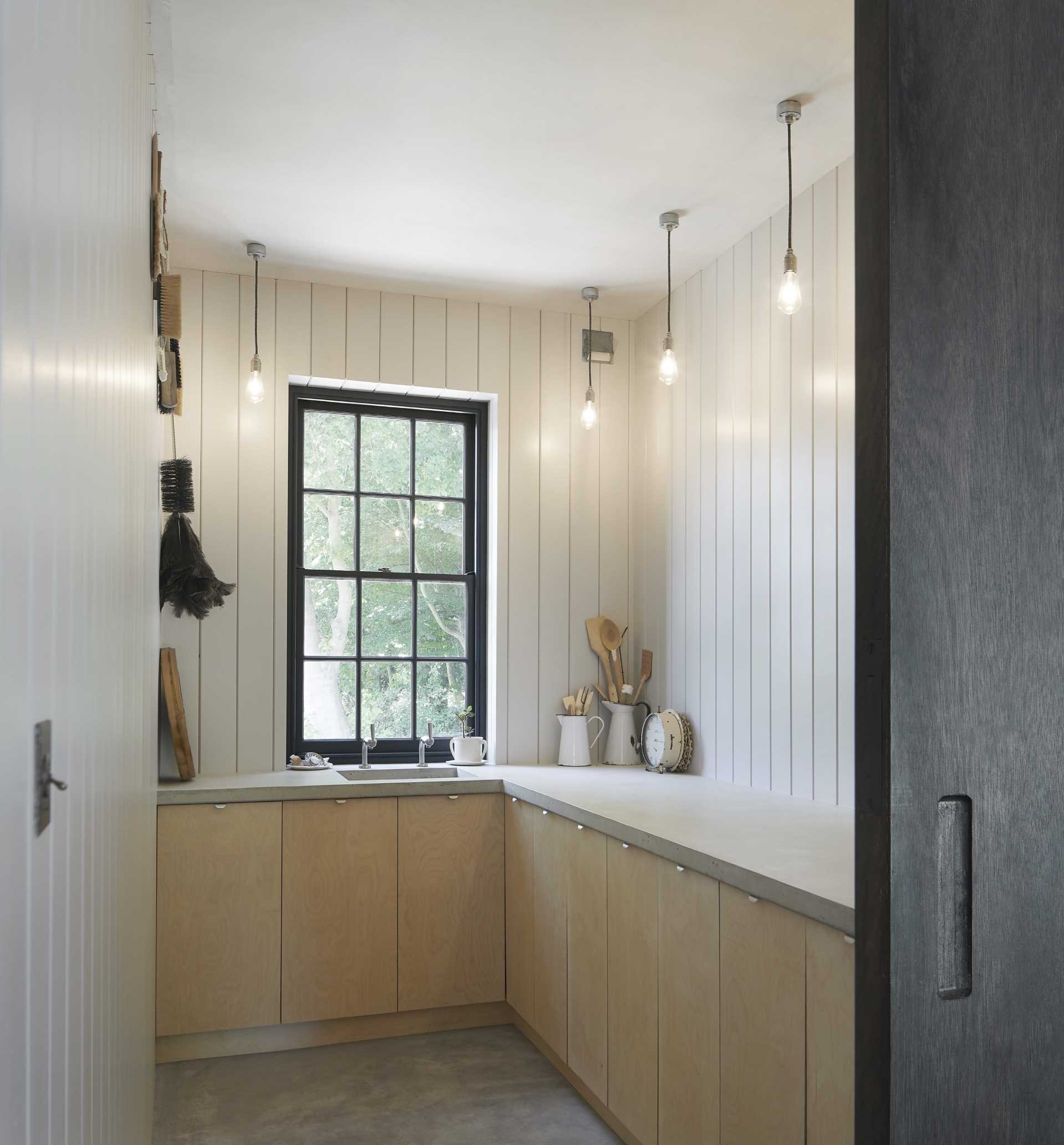 A contemporary pantry with white paneled walls and black window frame.