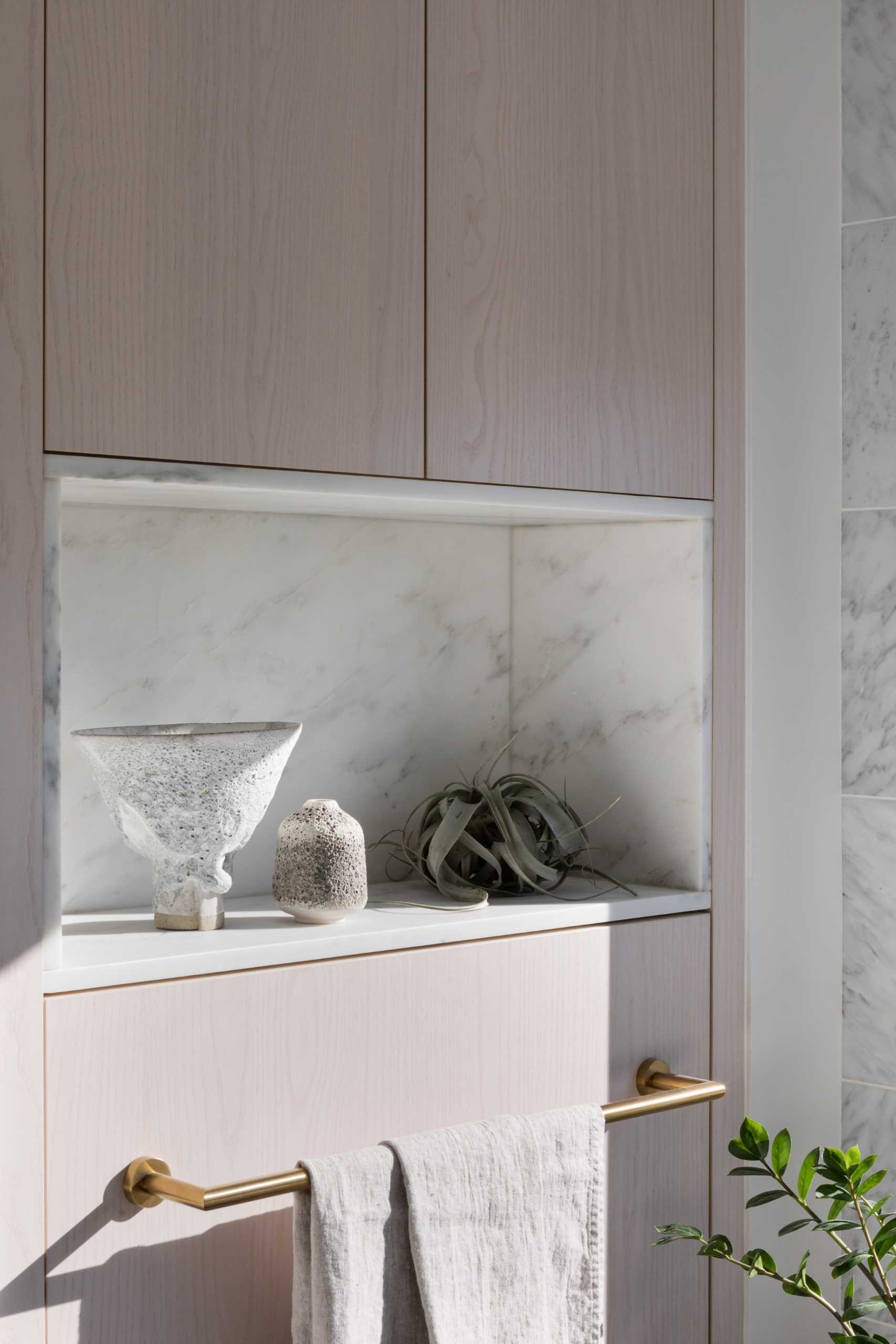 A modern bathroom with light wood cabinets and a marble lined niche.