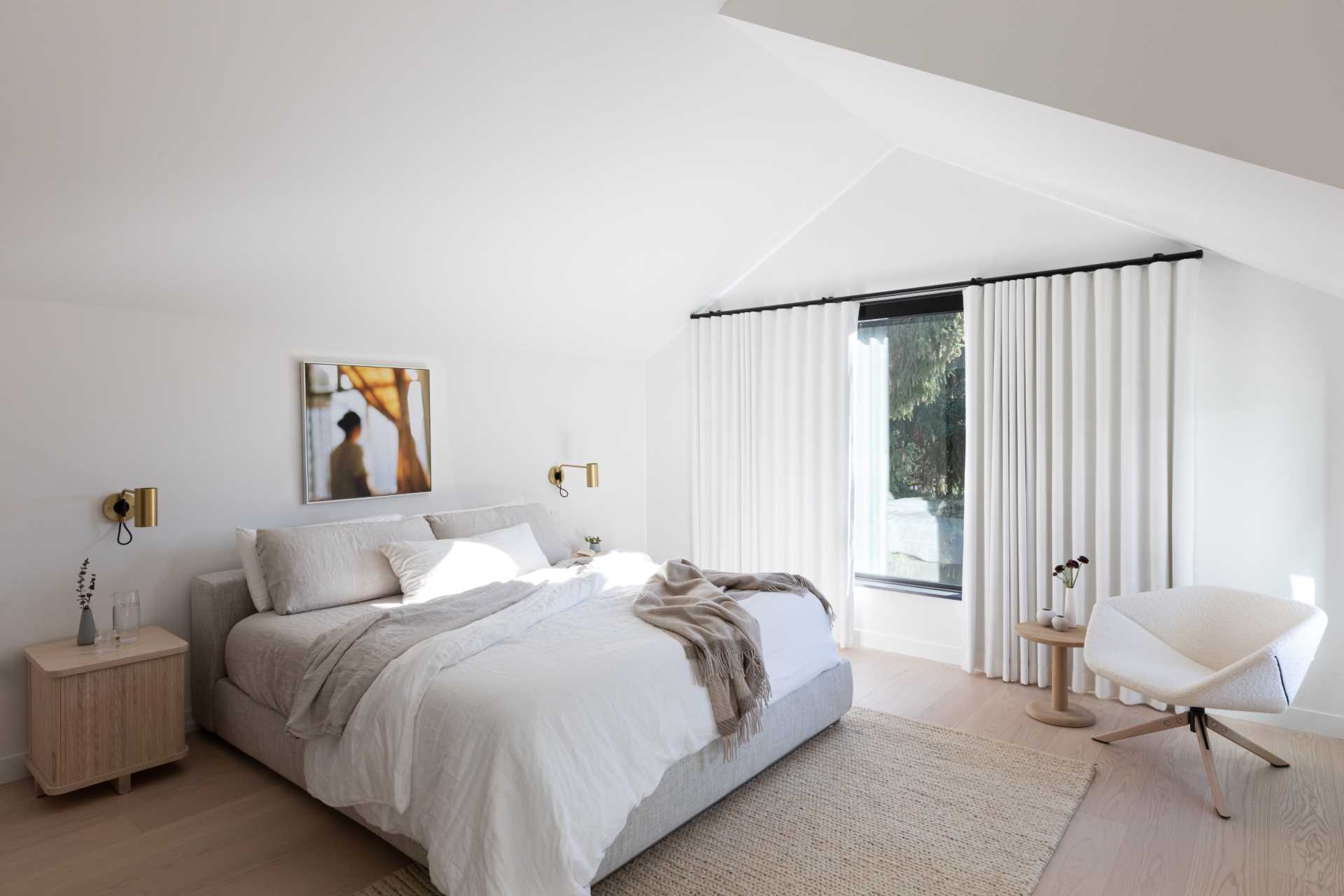In this modern primary bedroom, a vaulted ceiling and white walls create a large yet calming space.