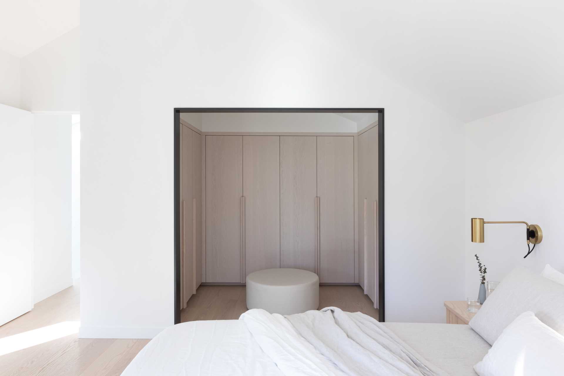 A modern bedroom with an open walk-in closet with light wood cabinets.