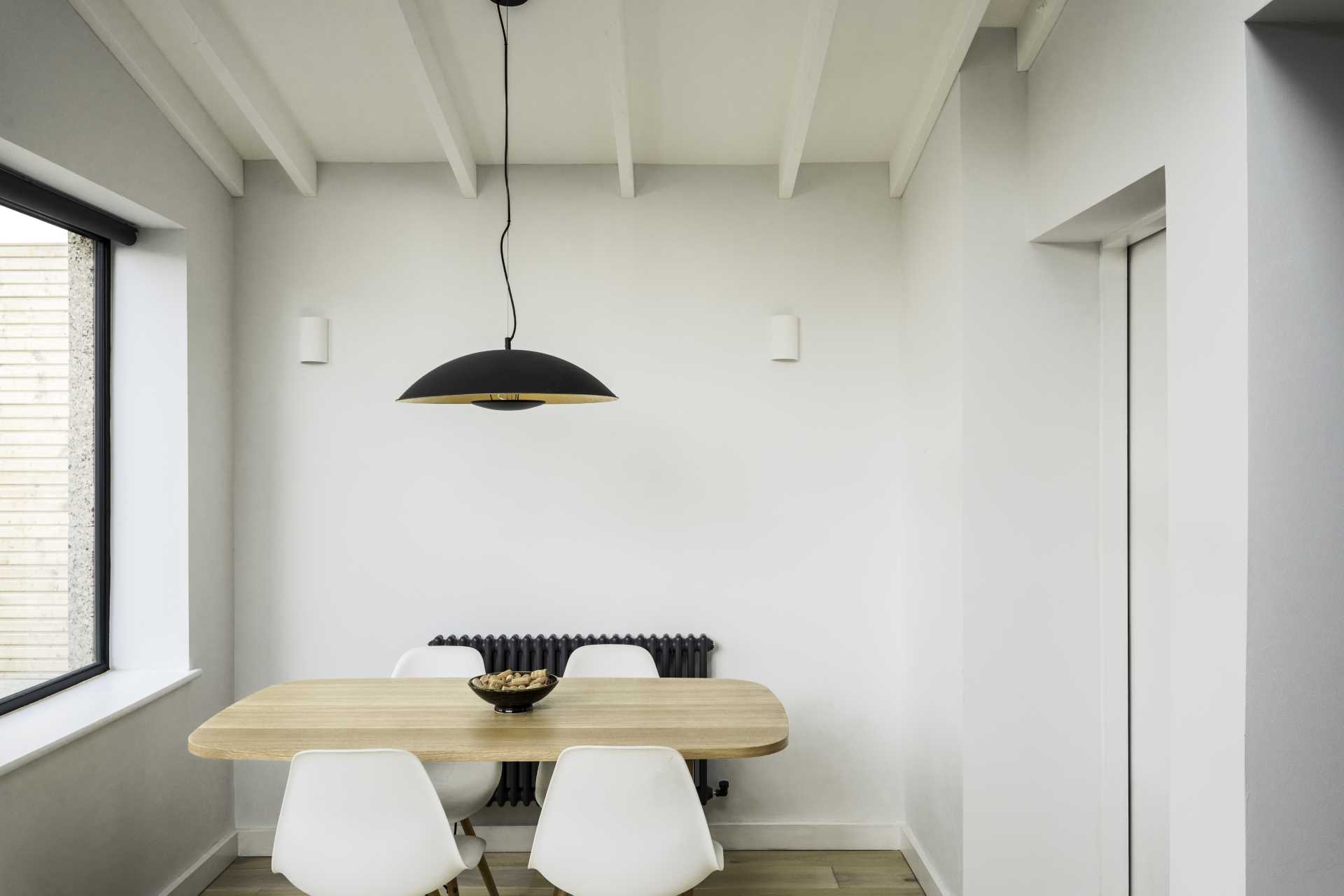 A small dining area with a wood table and a black pendant light above.