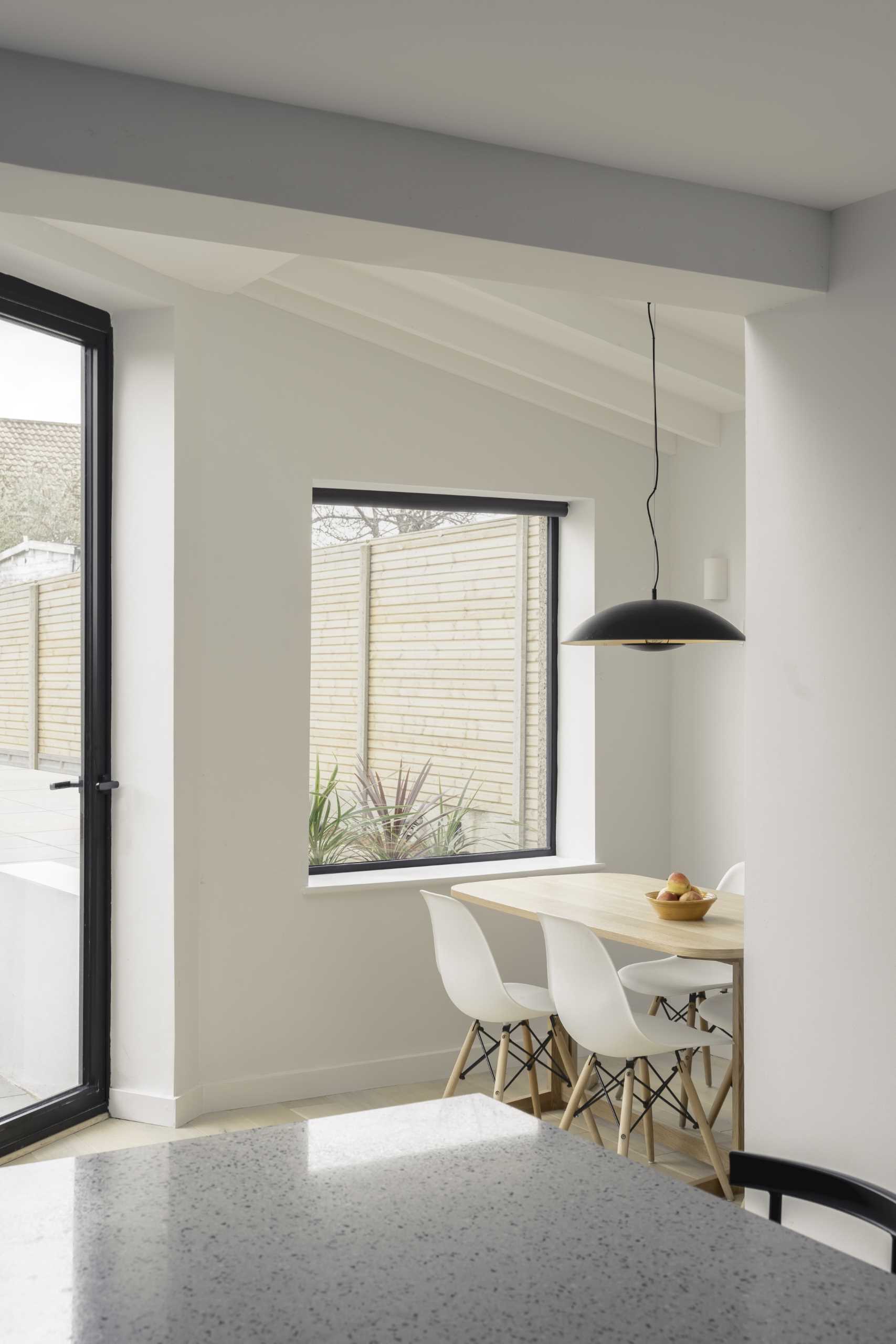 A small dining area with a wood table and a black pendant light above.