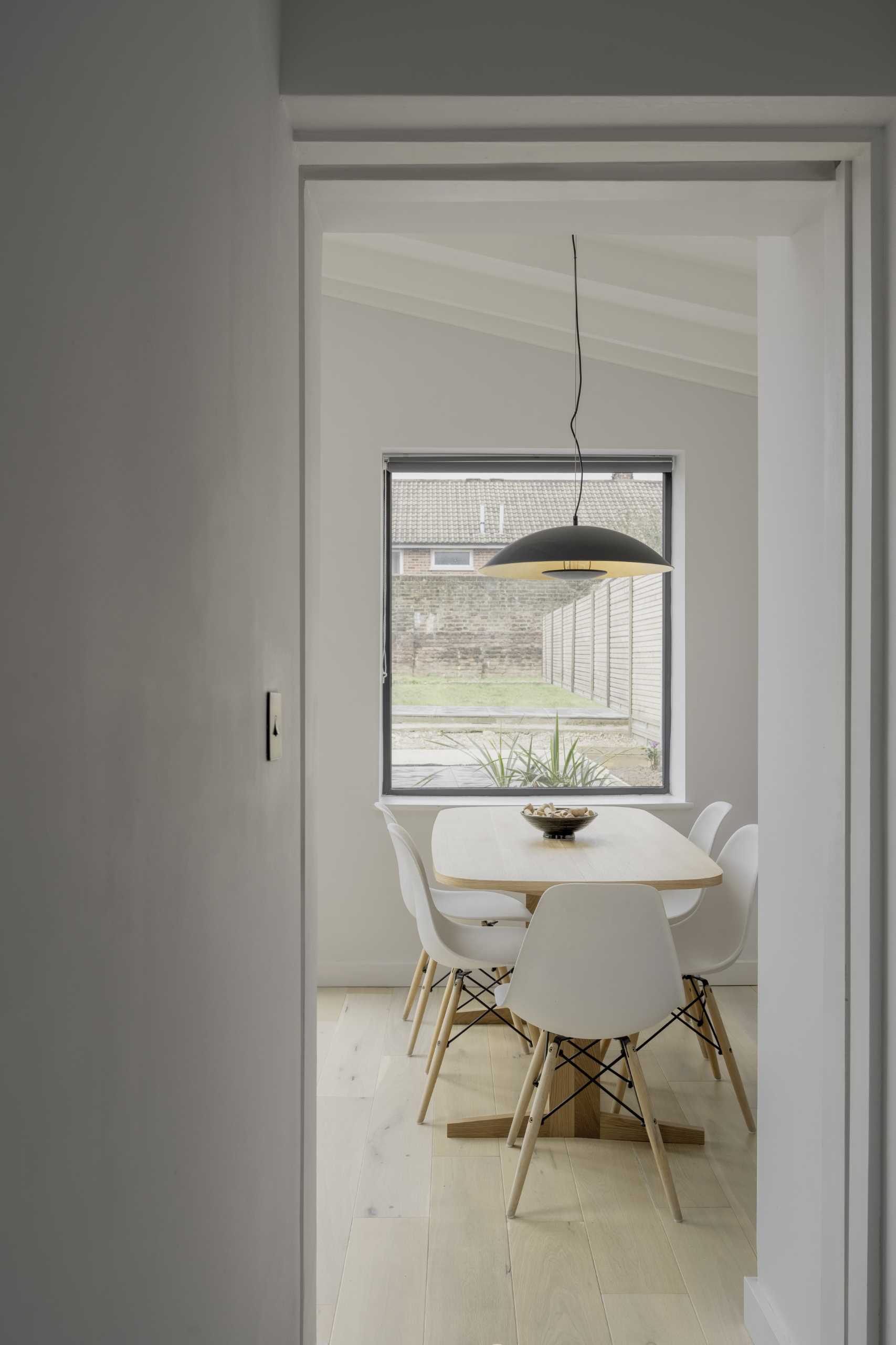 A small dining area with a wood table and a black pendant light above.