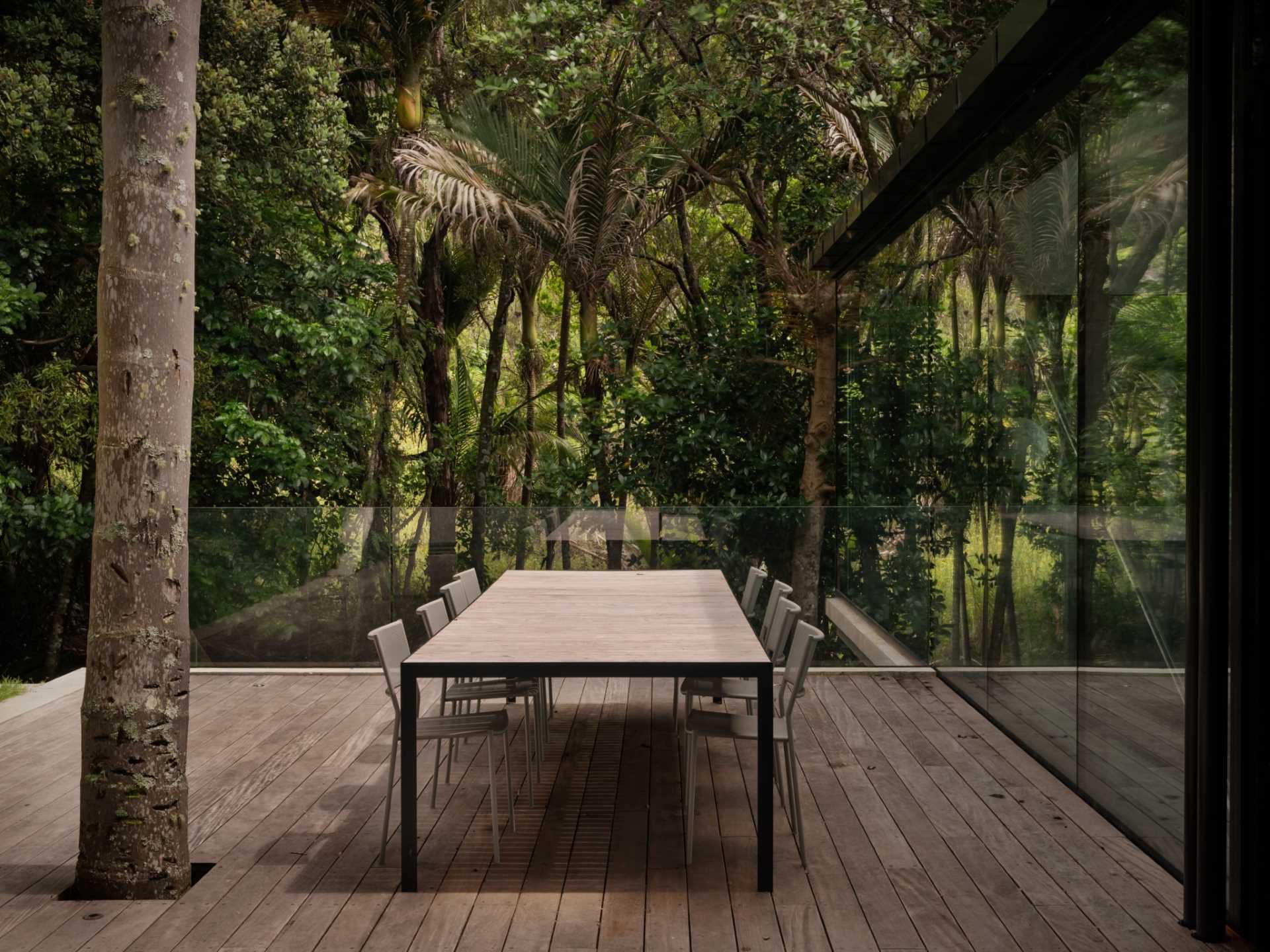 Sliding glass doors on either side of the kitchen of this modern home, open to outdoor spaces, like a wood deck that's furnished for outdoor dining under the trees.