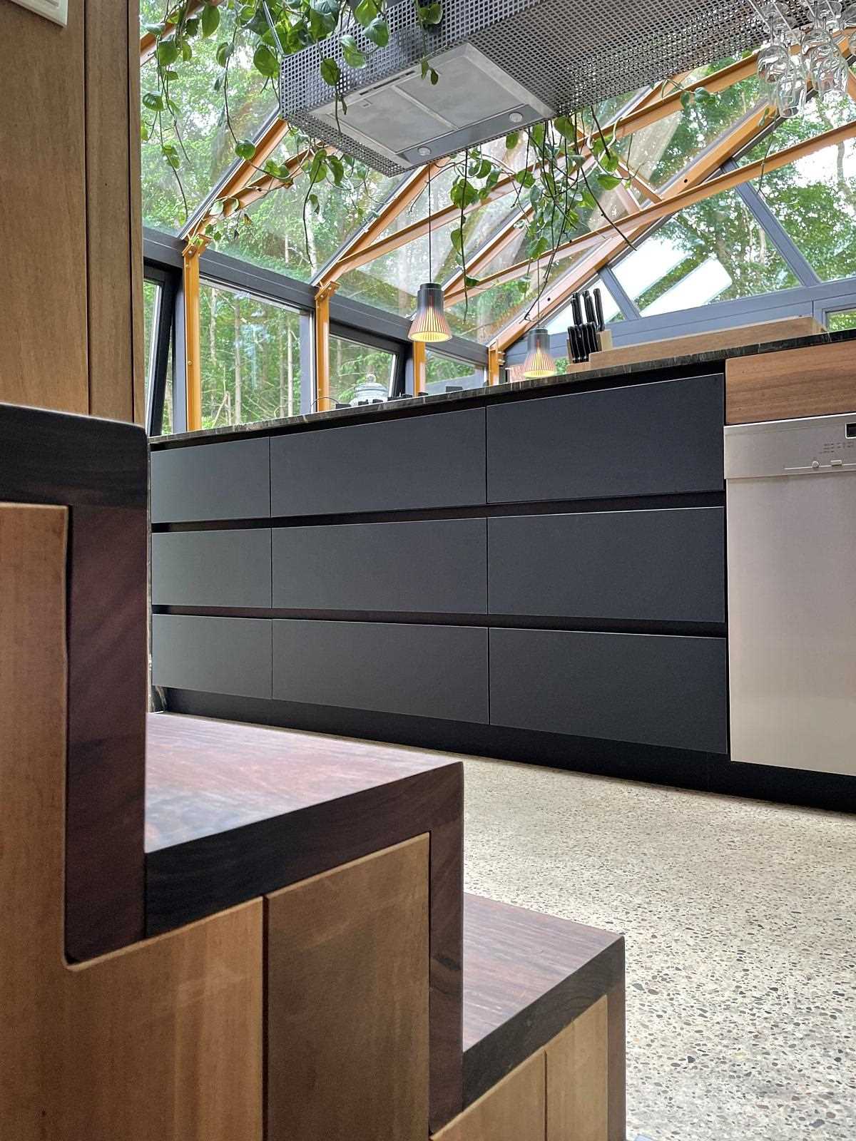 A modern kitchen with black cabinets and wood stairs.