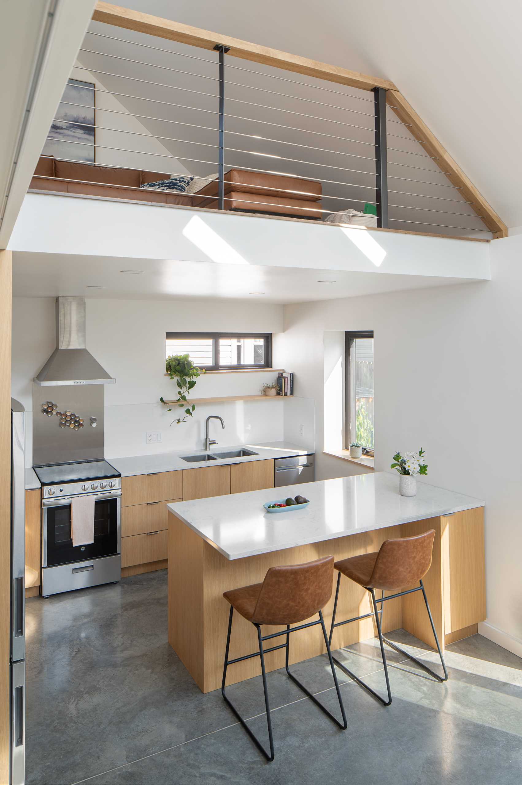 A modern kitchen with wood cabinetry and white countertops. Multiple windows allow natural light to fill the space.