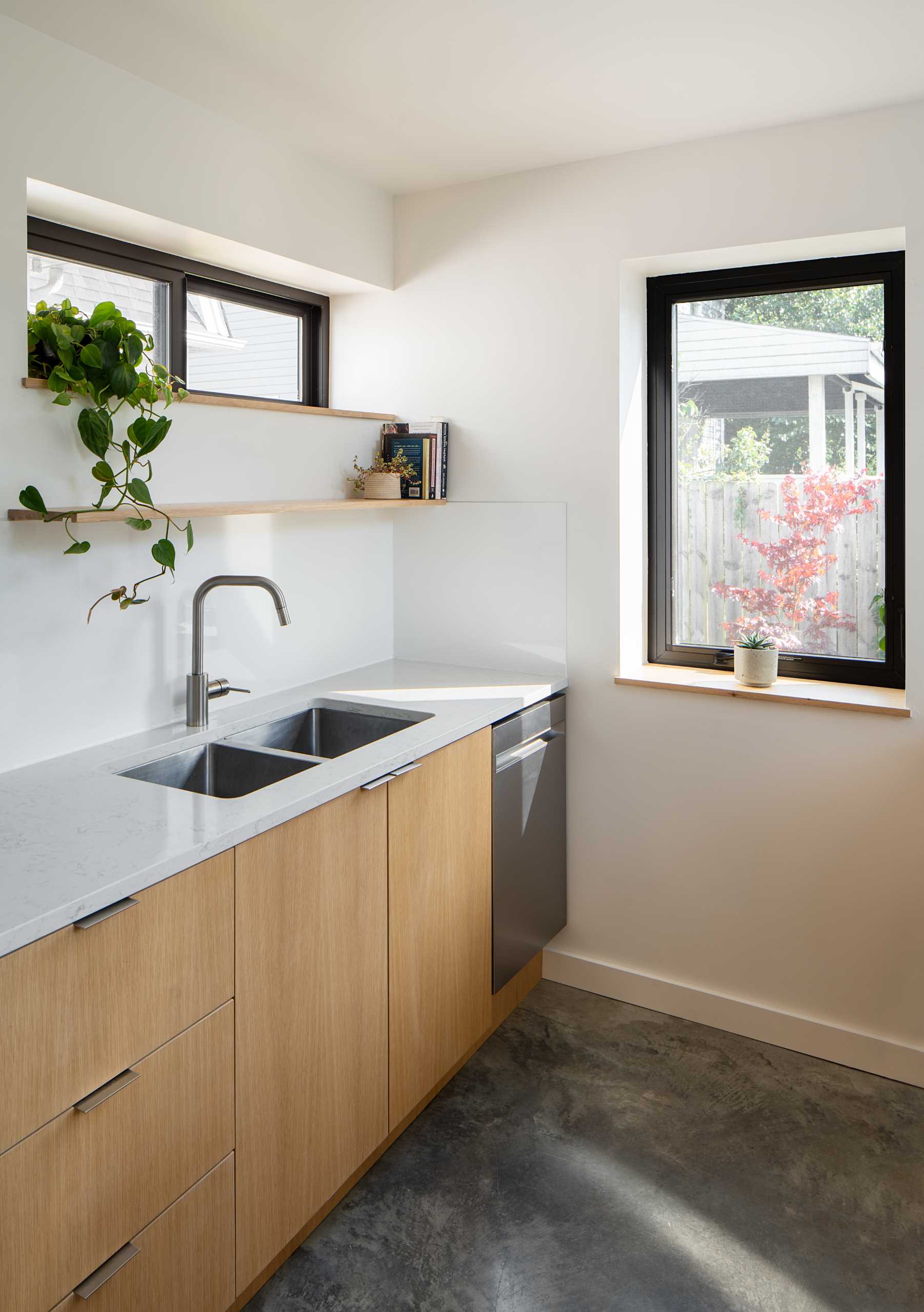 A modern kitchen with wood cabinetry and white countertops. Multiple windows allow natural light to fill the space.