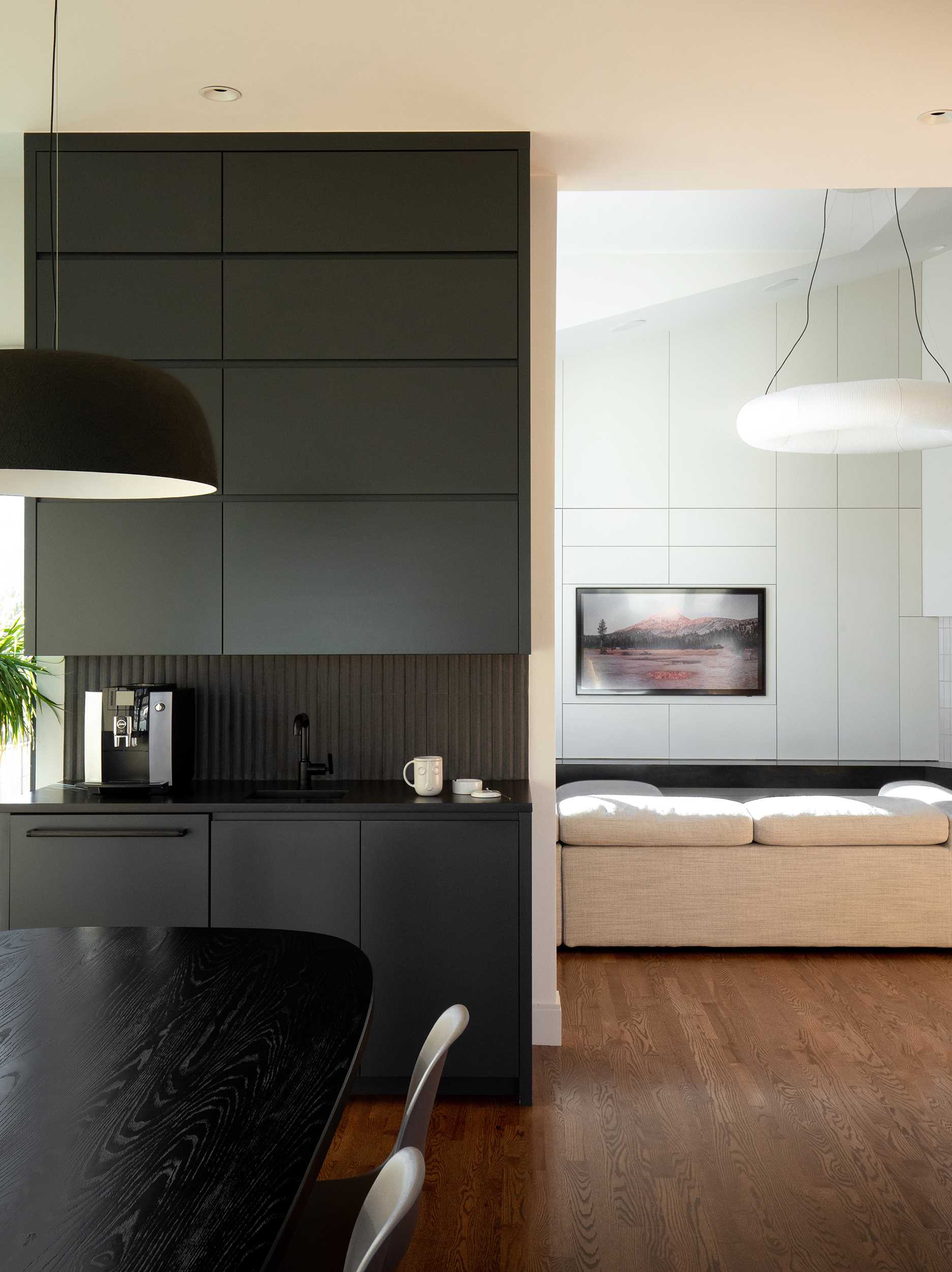 This modern wet bar, with its black finish, features a trash / recycle / paper towel pullout by the sink, refrigerator drawers below, tiered hidden storage above for glassware, and a coffee maker.