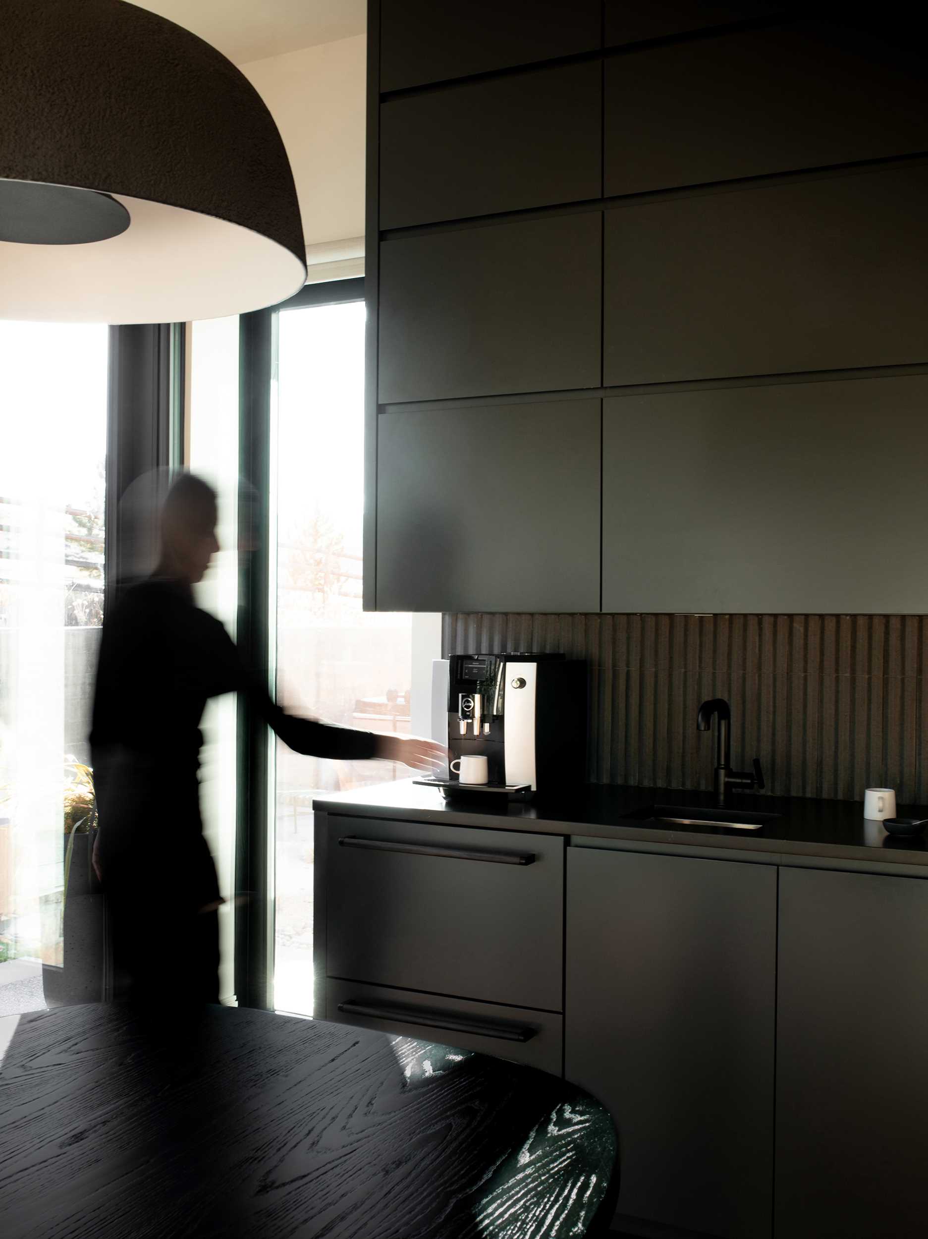 This modern wet bar, with its black finish, features a trash / recycle / paper towel pullout by the sink, refrigerator drawers below, tiered hidden storage above for glassware, and a coffee maker.