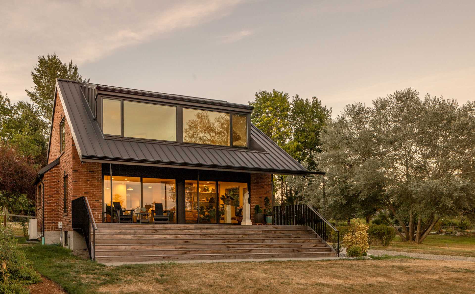 An updated brick home includes a sloping black metal roof, while the porch has been expanded to replace the small rear deck with a large outdoor space that spans both the new living room and dining room.
