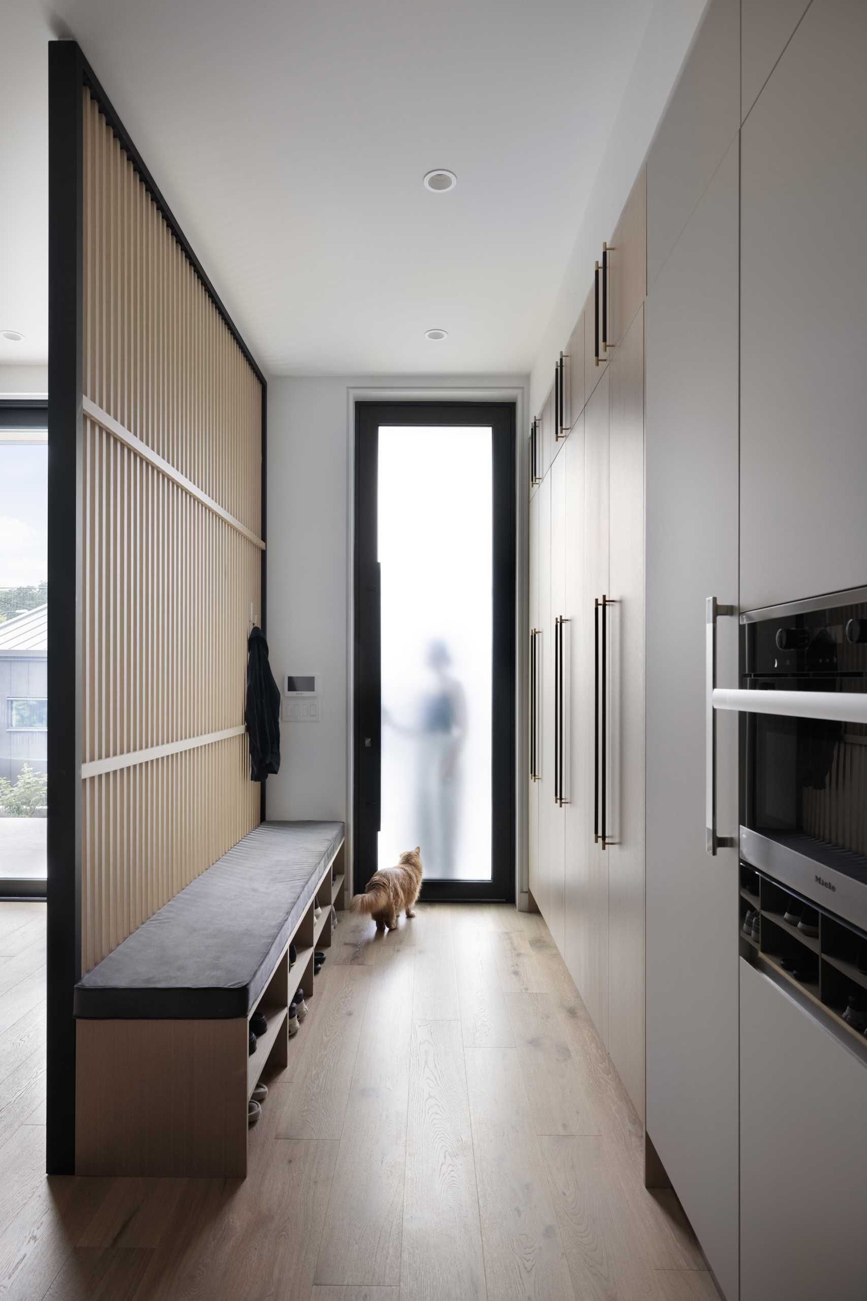 A small mudroom with a wood partition wall, floor-to-ceiling cabinets, and a long bench with shoe storage underneath.