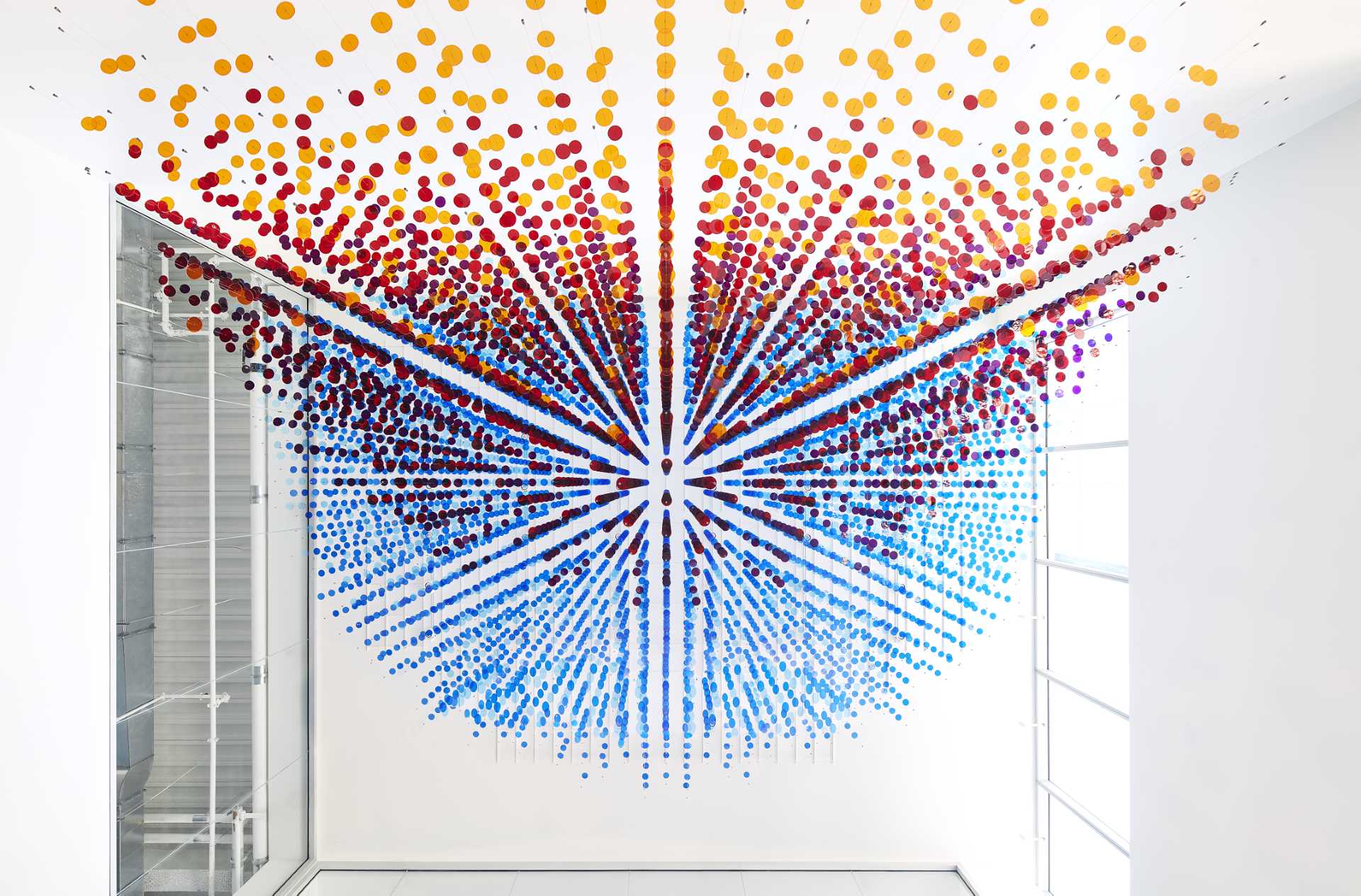 A custom art installation in a lobby atrium is made from 8,000 colorful discs suspended from 650 wire cables.