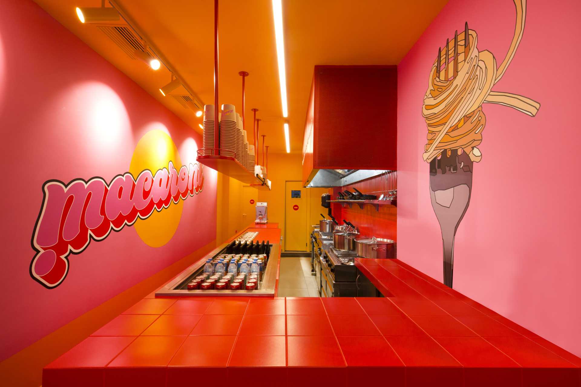 Upon entering this pasta shop, the customer faces the counter and has a full view of the open kitchen. The playful combo of red, pink, and orange colors turns this limited space into a vibrant, funky area.