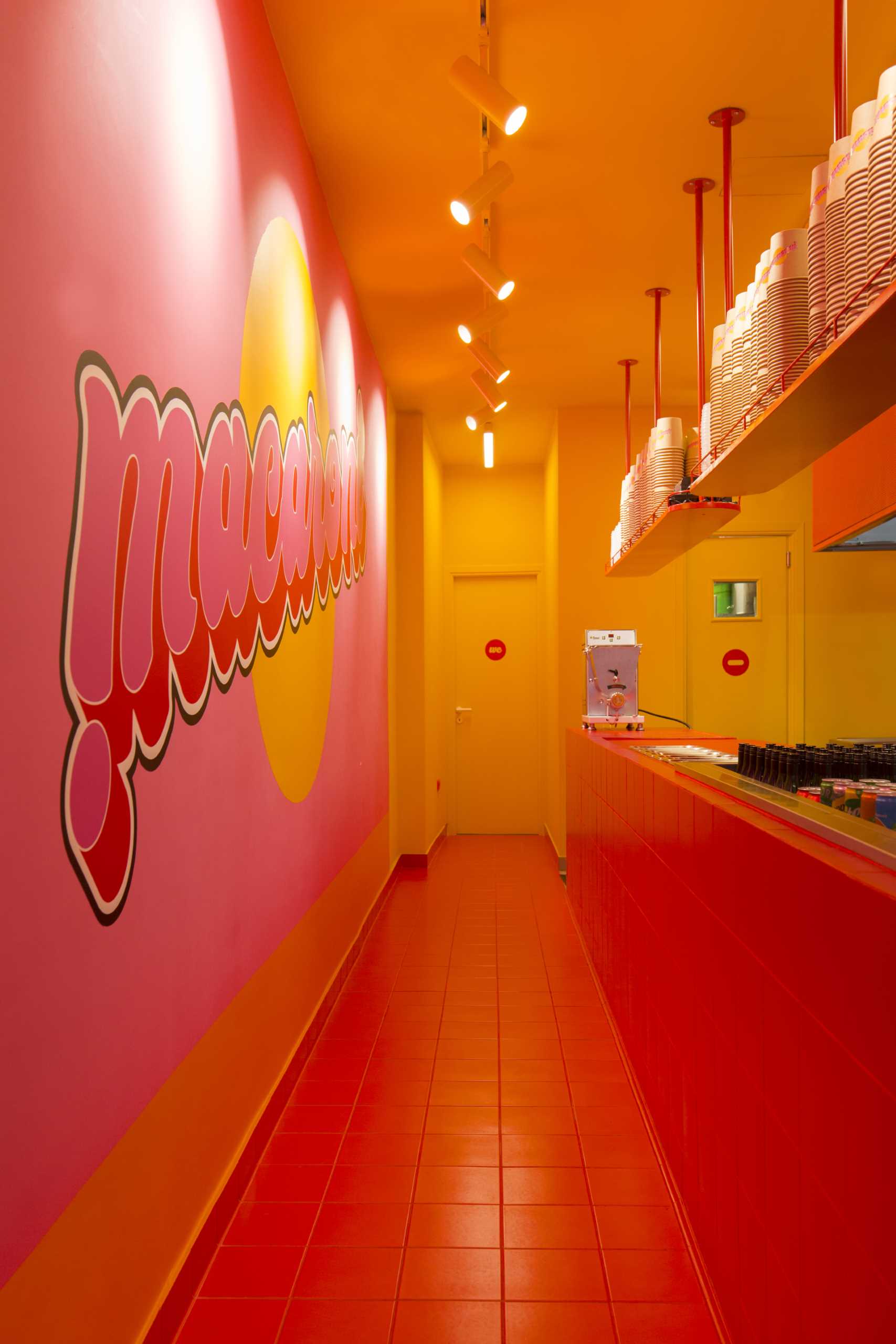 Upon entering this pasta shop, the customer faces the counter and has a full view of the open kitchen. The playful combo of red, pink, and orange colors turns this limited space into a vibrant, funky area.