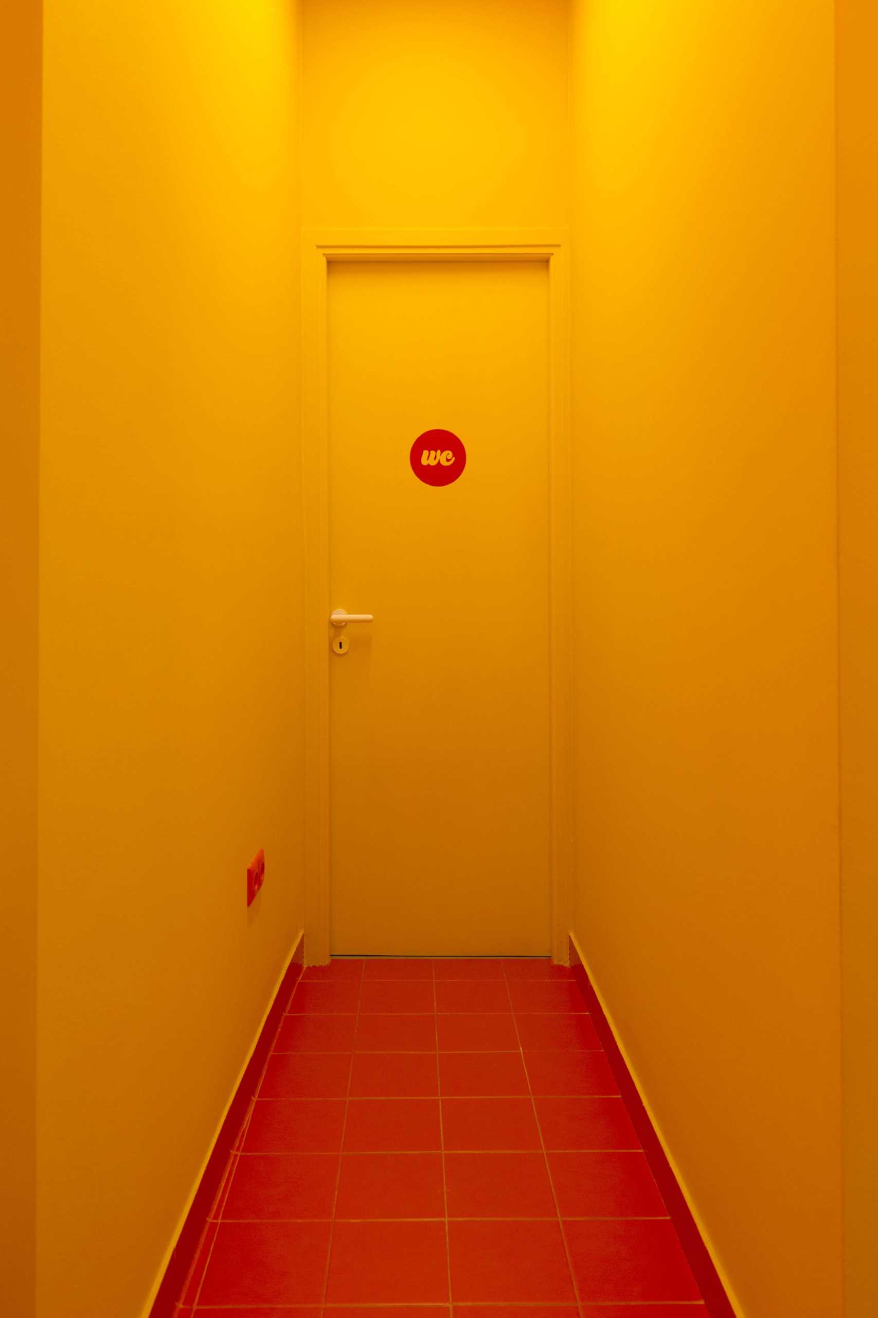 A yellow hallway that leads to the bathroom of a pasta shop.