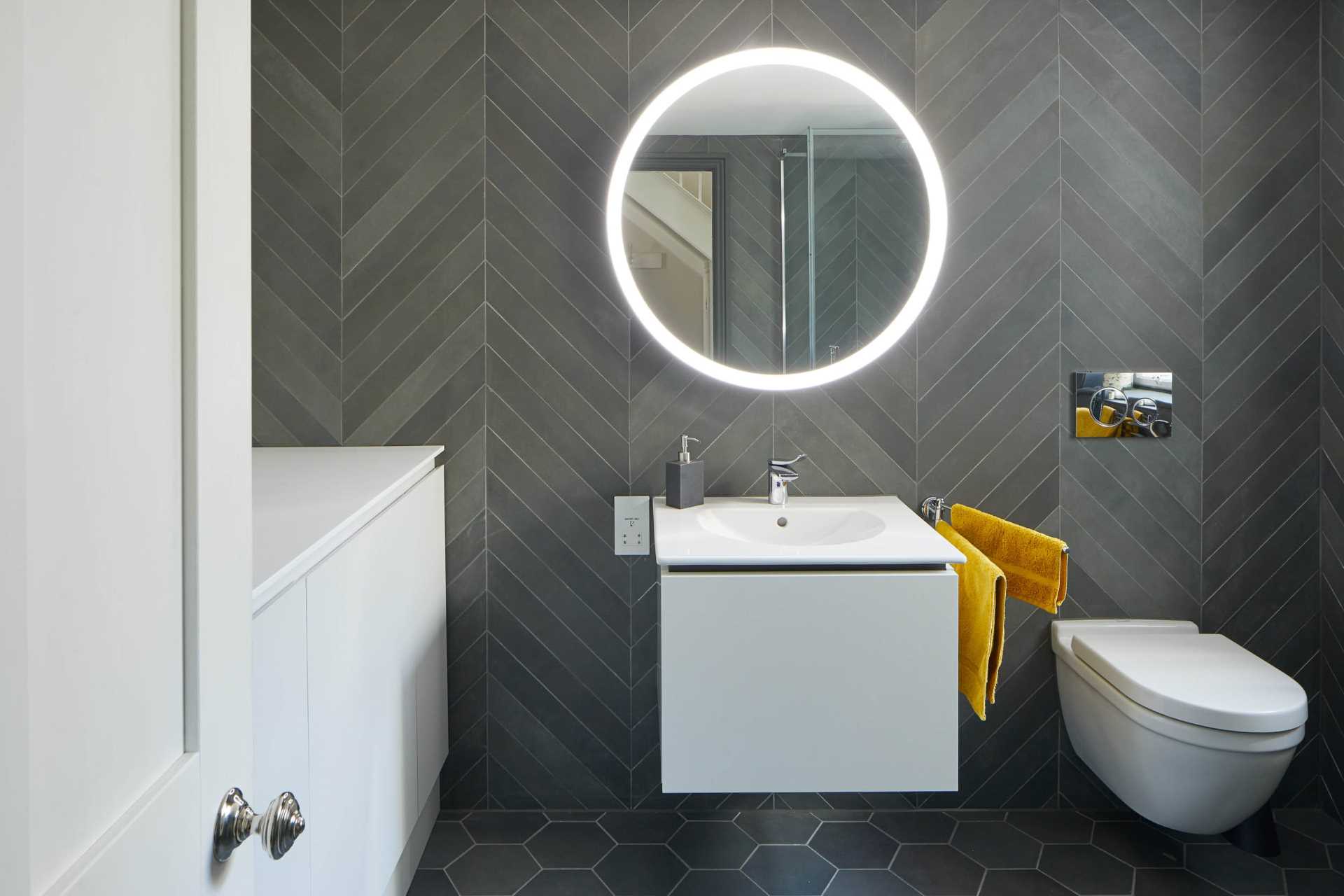 In this bathroom, the walls have been covered in grey tiles in a chevron pattern, while hexagonal tiles cover the floor.