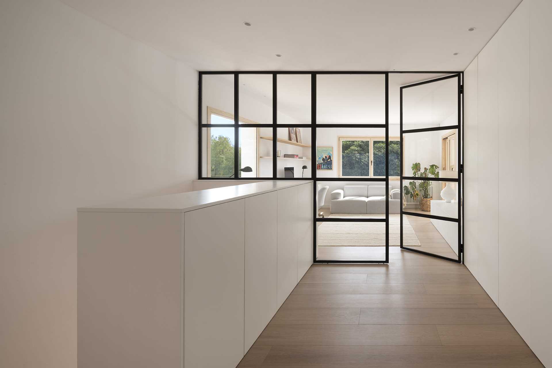 At the top of the stairs, there's a black-framed glass-enclosed home office with a desk and couch.