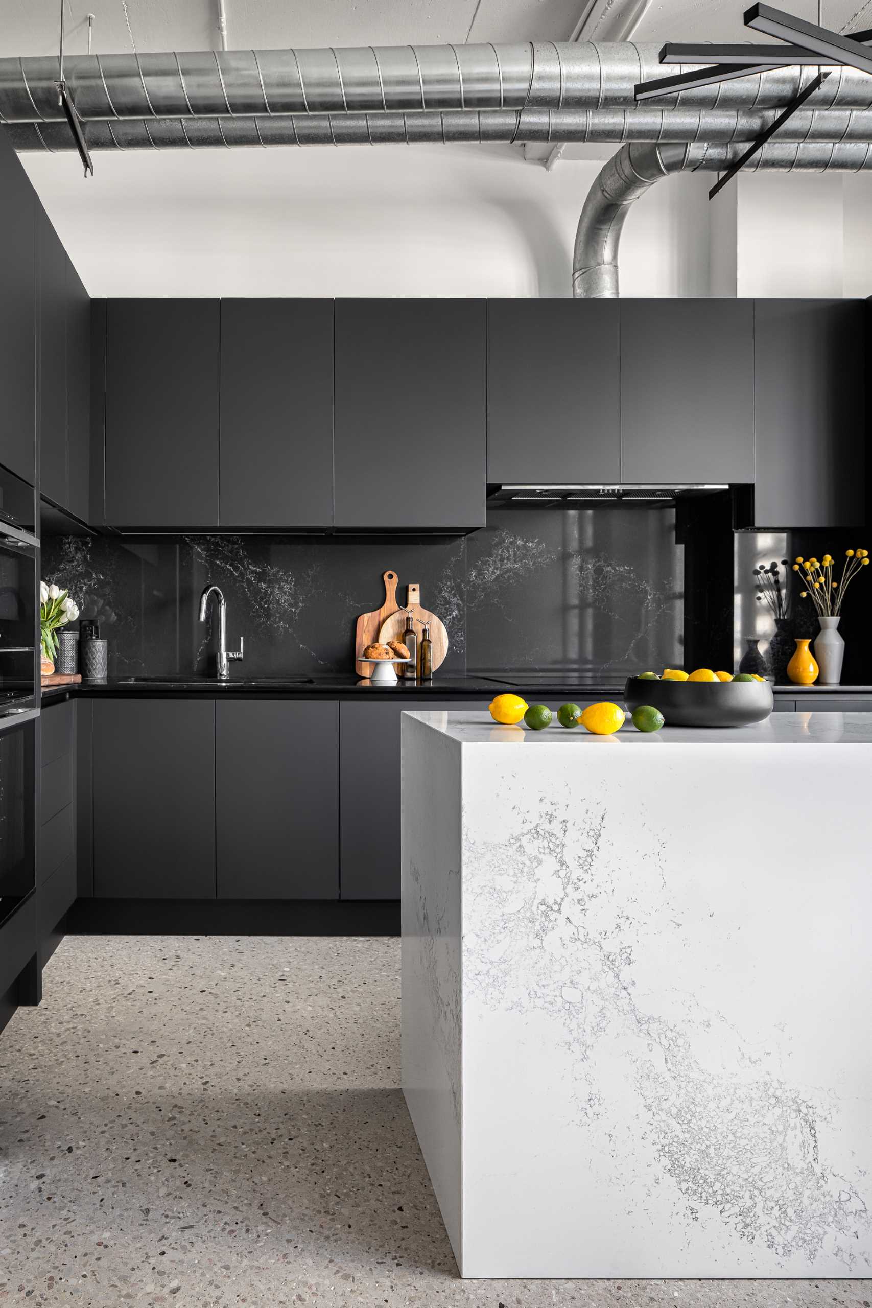 A modern kitchen with a white stone island with subtle veins and minimalist hardware-free black cabinets.
